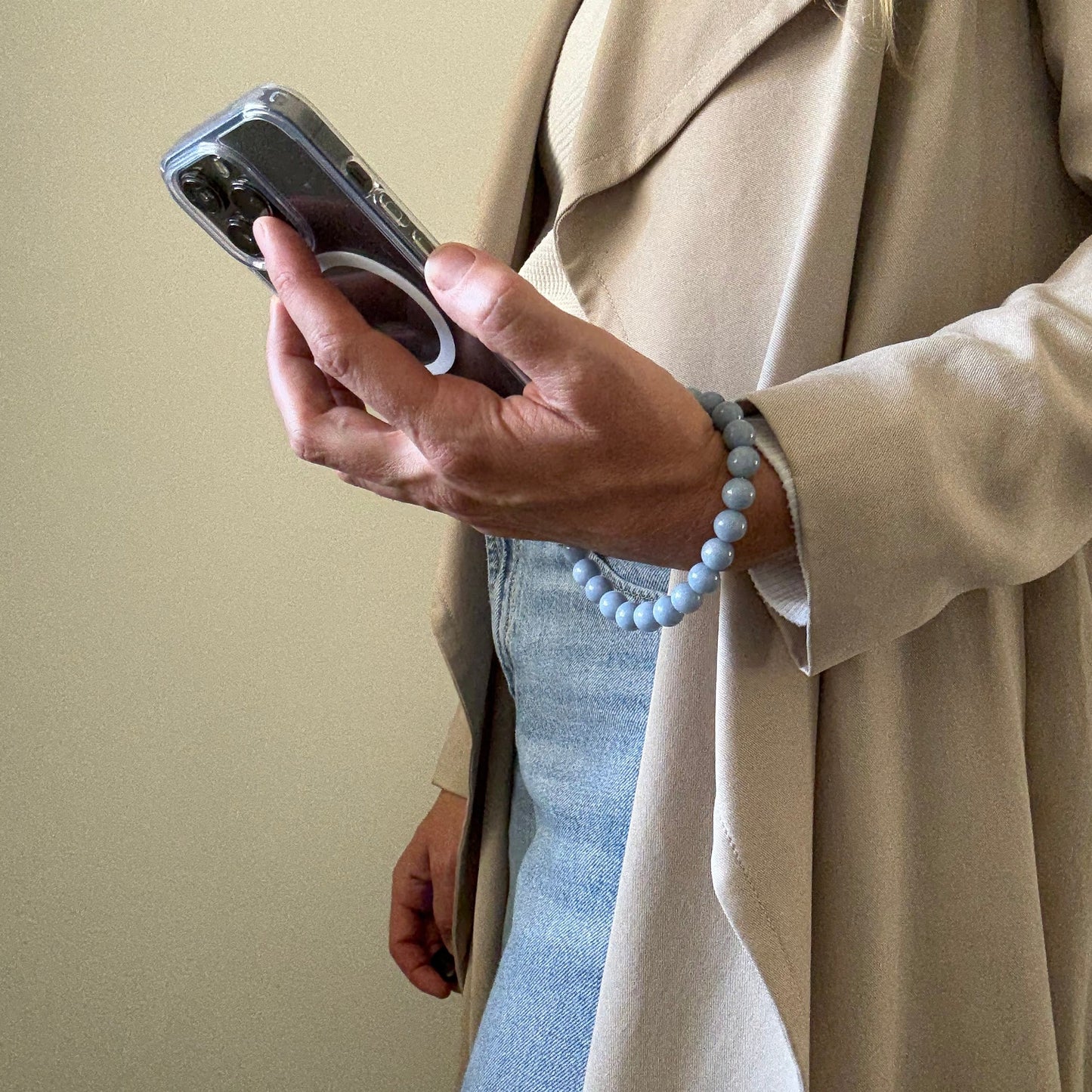 Person holding a blue beaded mobile phone chain with a beige background