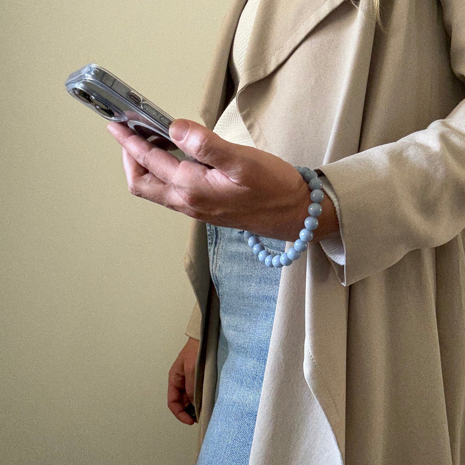 Person wearing a beige garment holding a blue beaded mobile phone chain with a blurred background