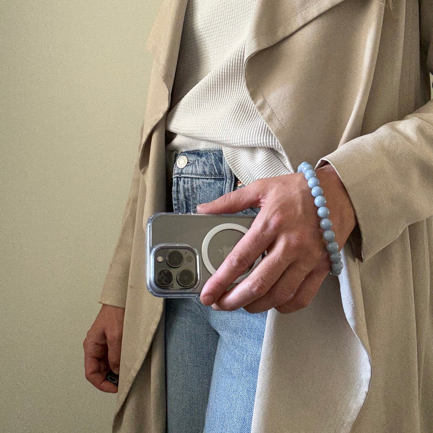 Person holding a smartphone with a blue beaded phone chain, and wearing a beige coat