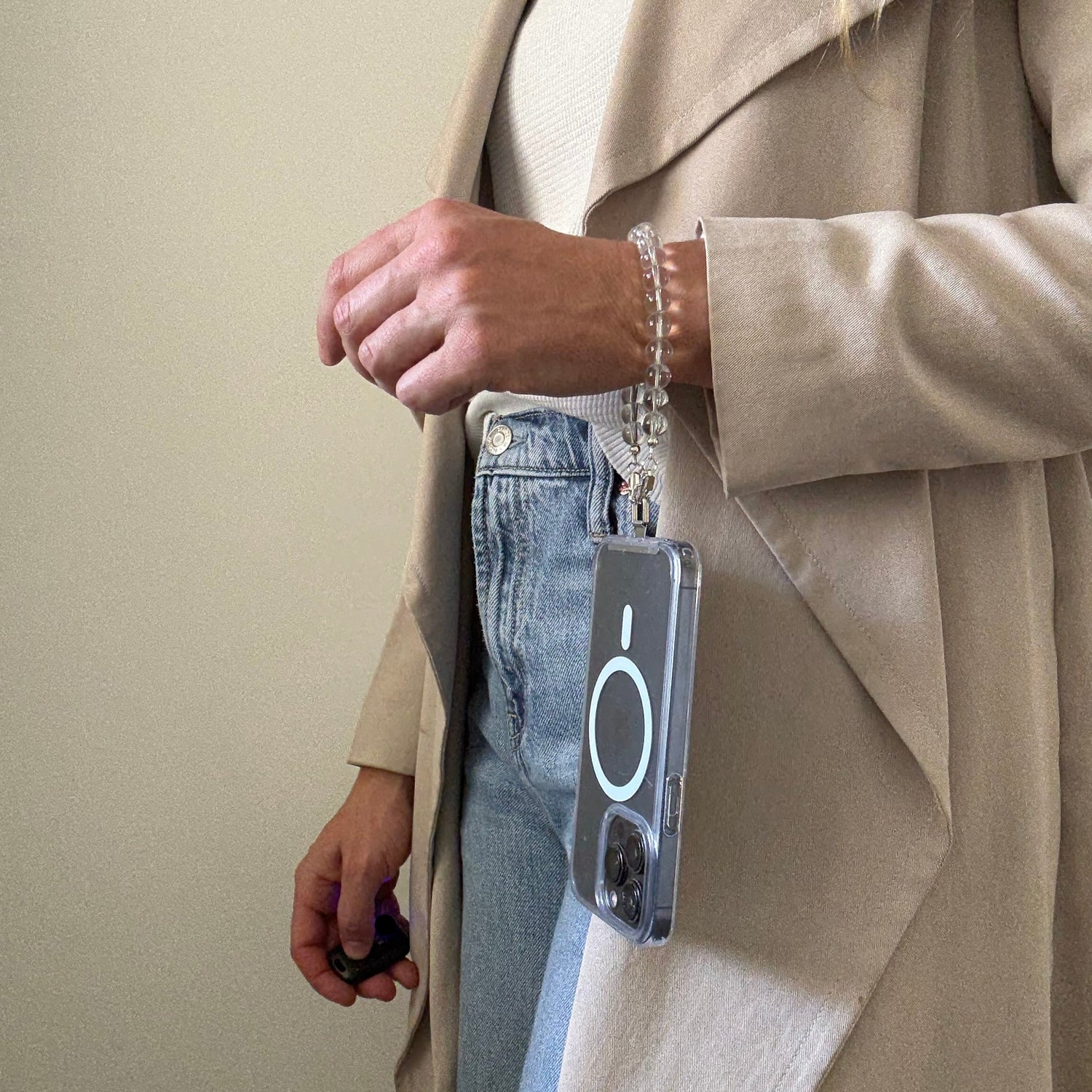 Person wearing a beige trench coat and blue jeans, holding a clear quartz crystal beaded phone chain.