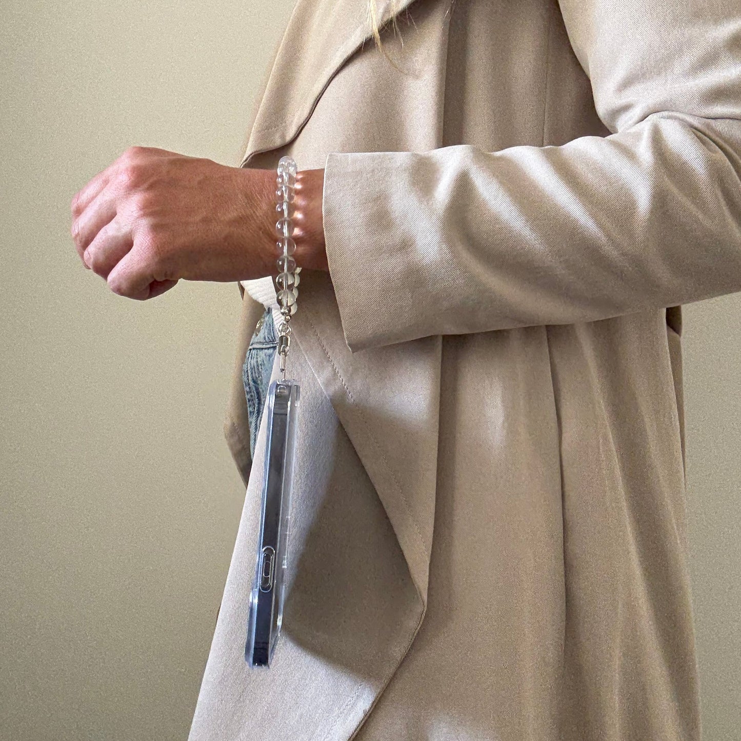 Person wearing a beige suit with a hand holding a smartphone with a beaded clear quartz crystal phone chain