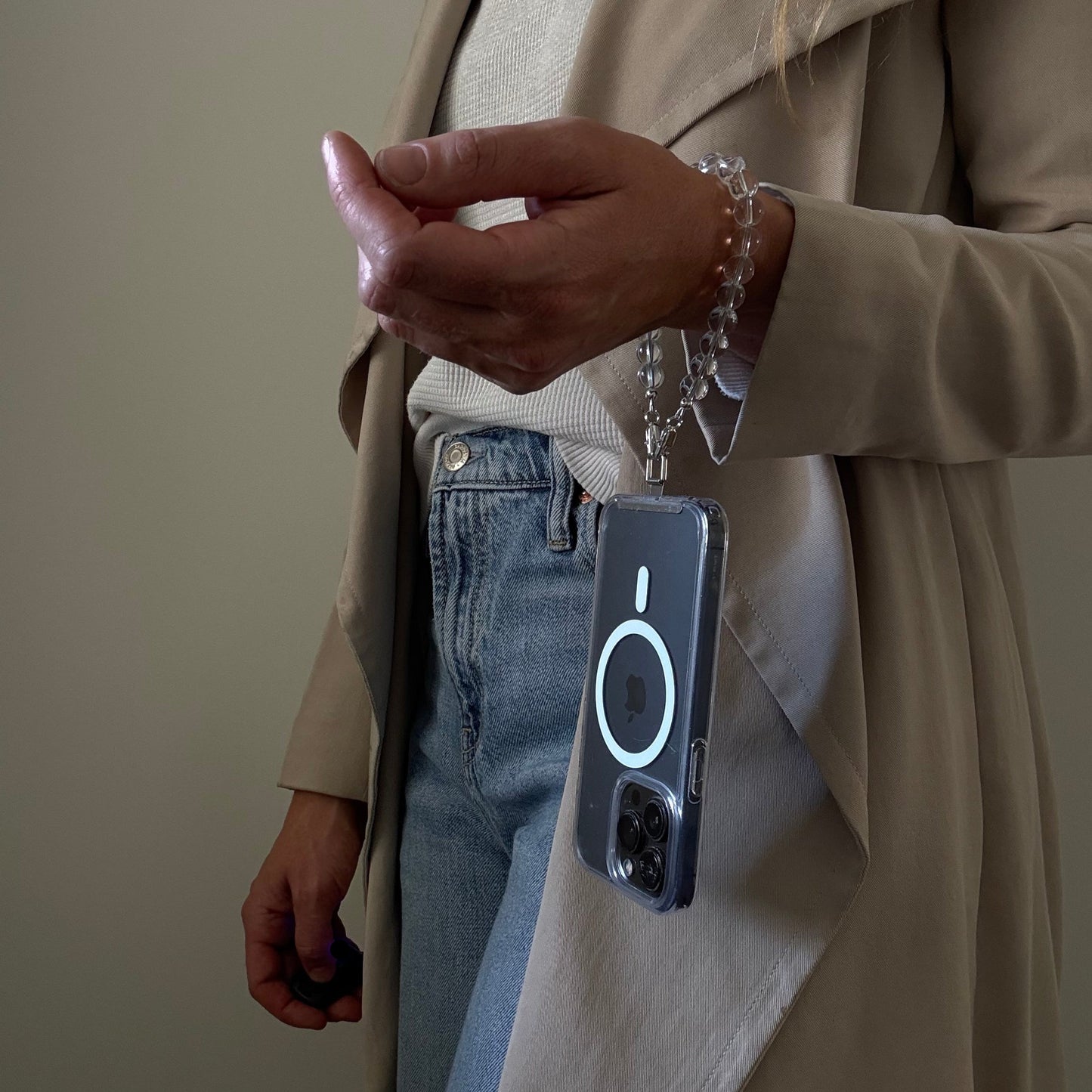 Person holding a smartphone with a beaded clear quartz crystal phone chain on a neutral background