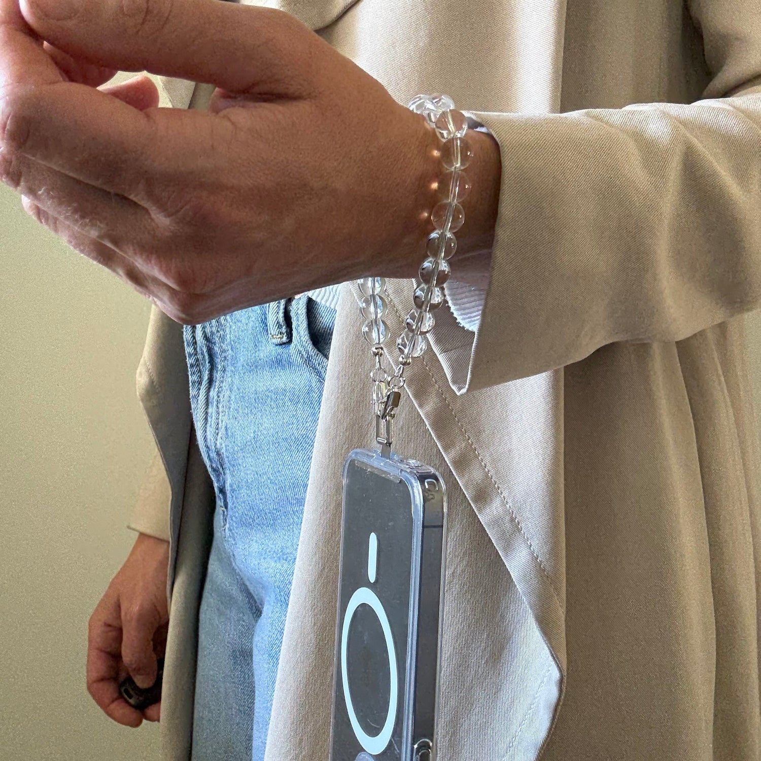 Person holding a smartphone with  a beaded clear quartz crystal phone chain against a light-colored surface.