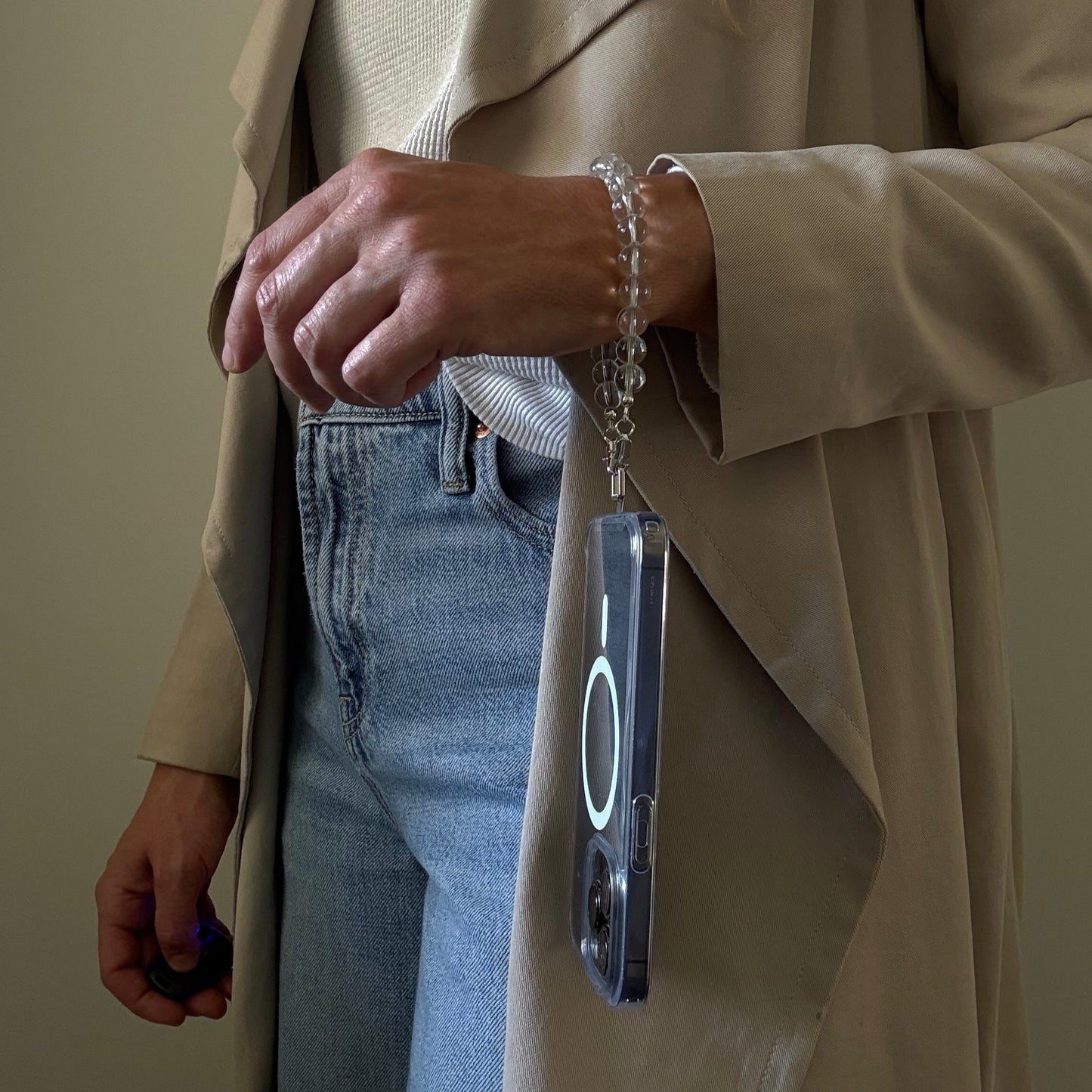 Person wearing a beige trench coat with a clear quartz crystal beaded phone chain