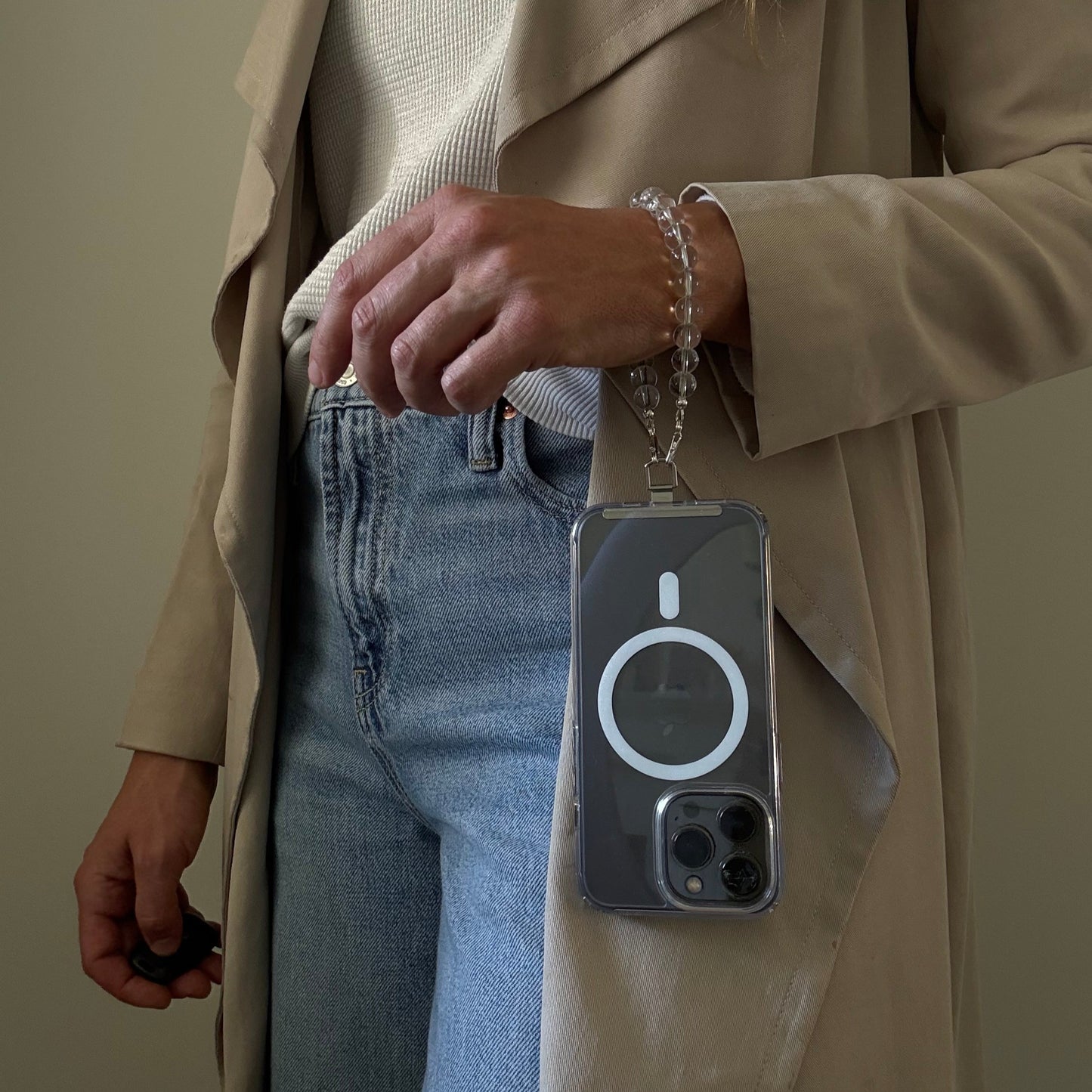Person wearing a beige trench coat and blue jeans, holding a clear quartz crystal beaded phone chain.