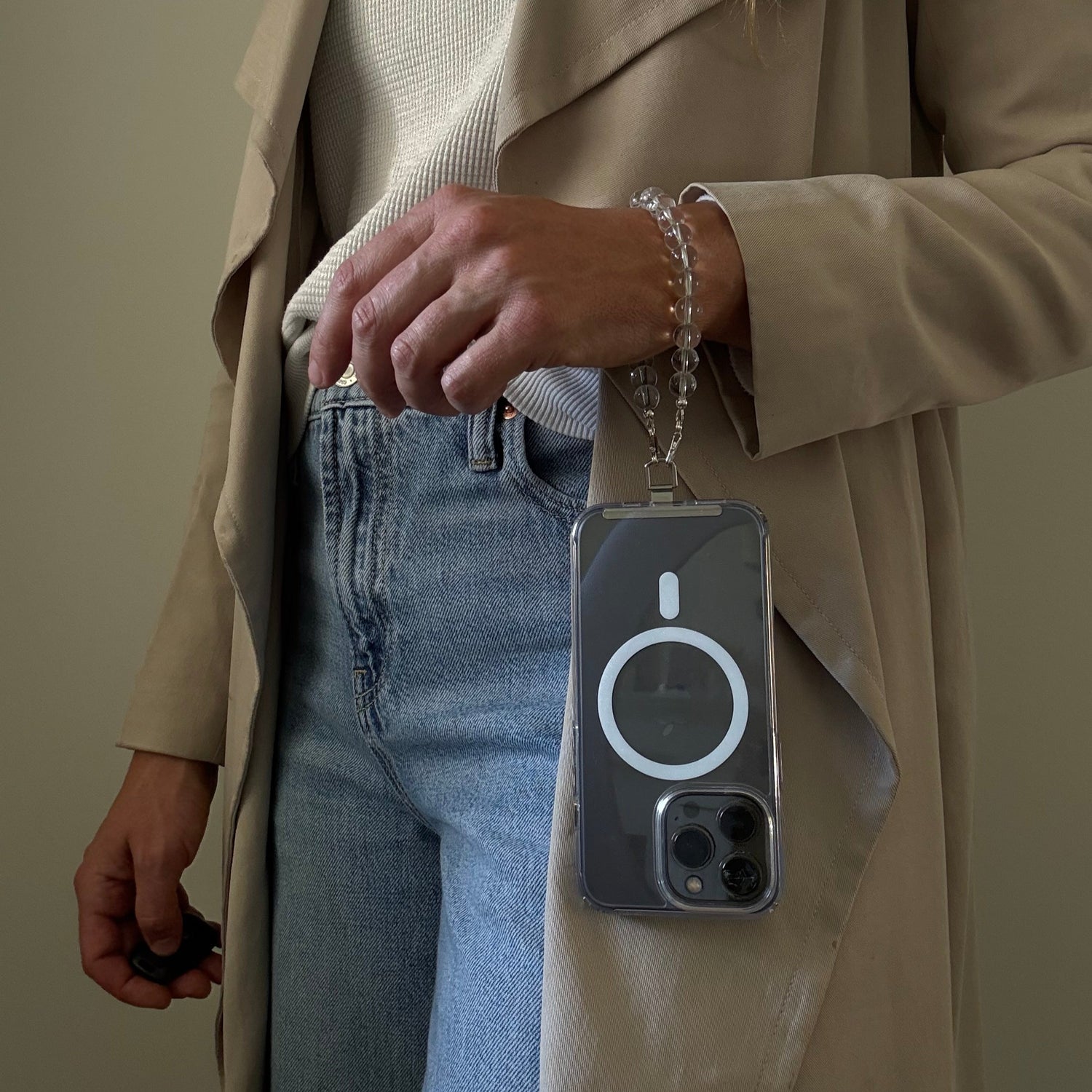 Person wearing a beige trench coat and blue jeans, holding a clear quartz crystal beaded phone chain.