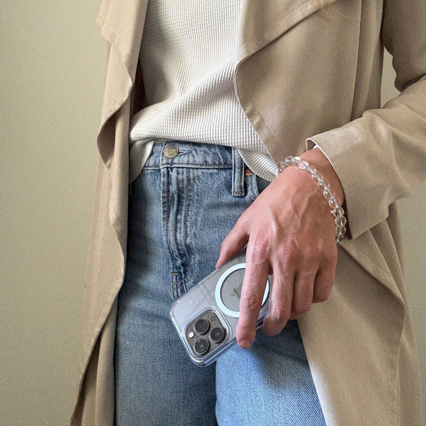 Person wearing a beige trench coat and blue jeans, holding a clear quartz crystal beaded phone chain.