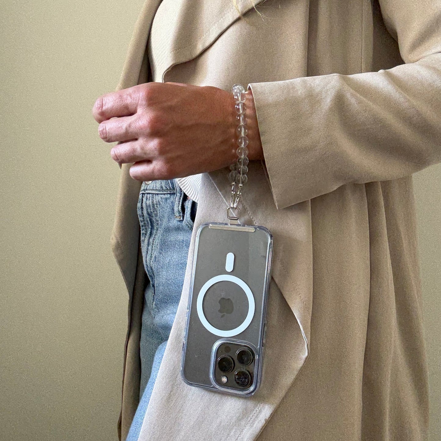 Person wearing a beige trench coat and blue jeans, holding a clear quartz crystal beaded phone chain.