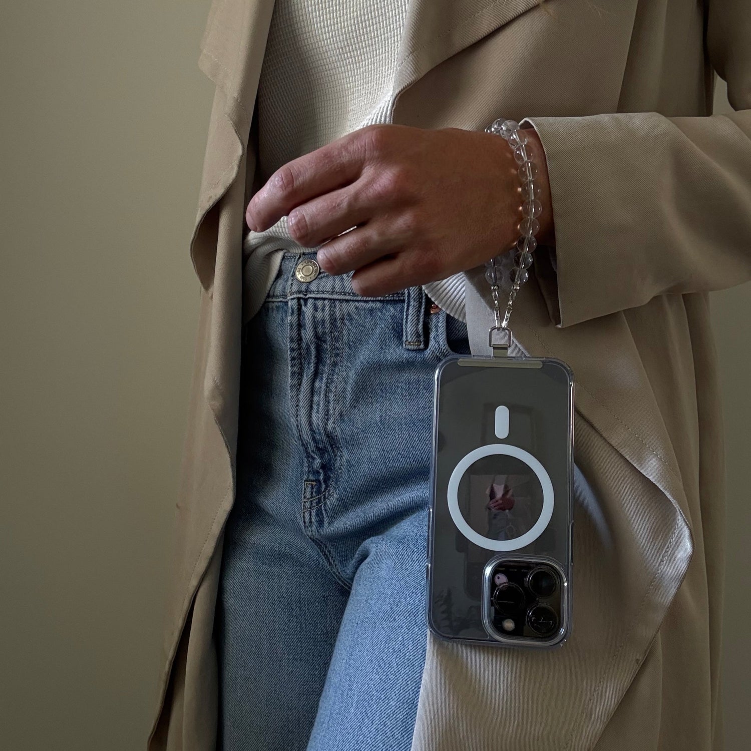 Person wearing a beige trench coat and blue jeans, holding a clear quartz crystal beaded phone chain.