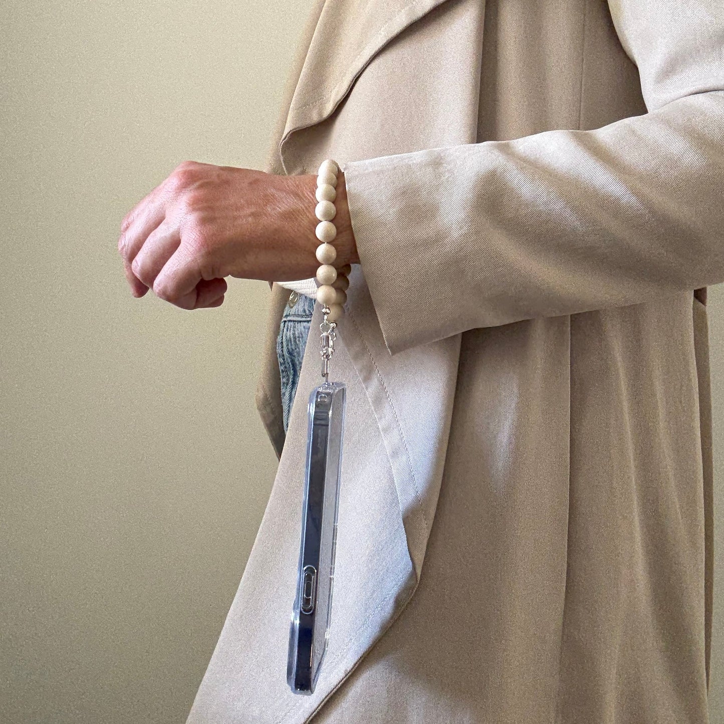 Person wearing a beige coat with a beaded fossil jasper phone chain on a plain background