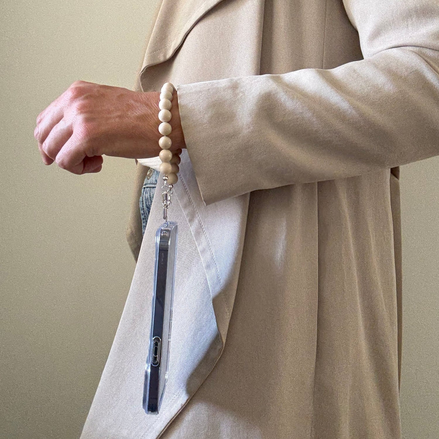 Person wearing a beige trench coat holding a beaded fossil jasper phone chain.