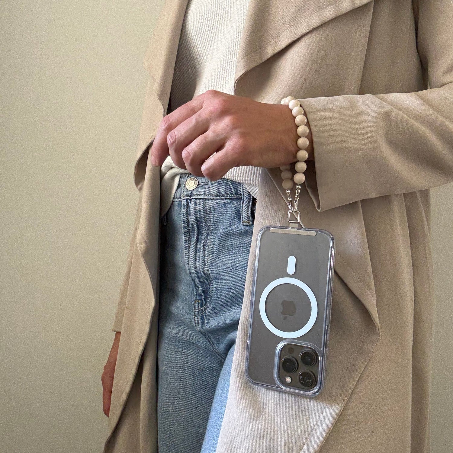Person wearing a beige trench coat with a beaded beige phone chain