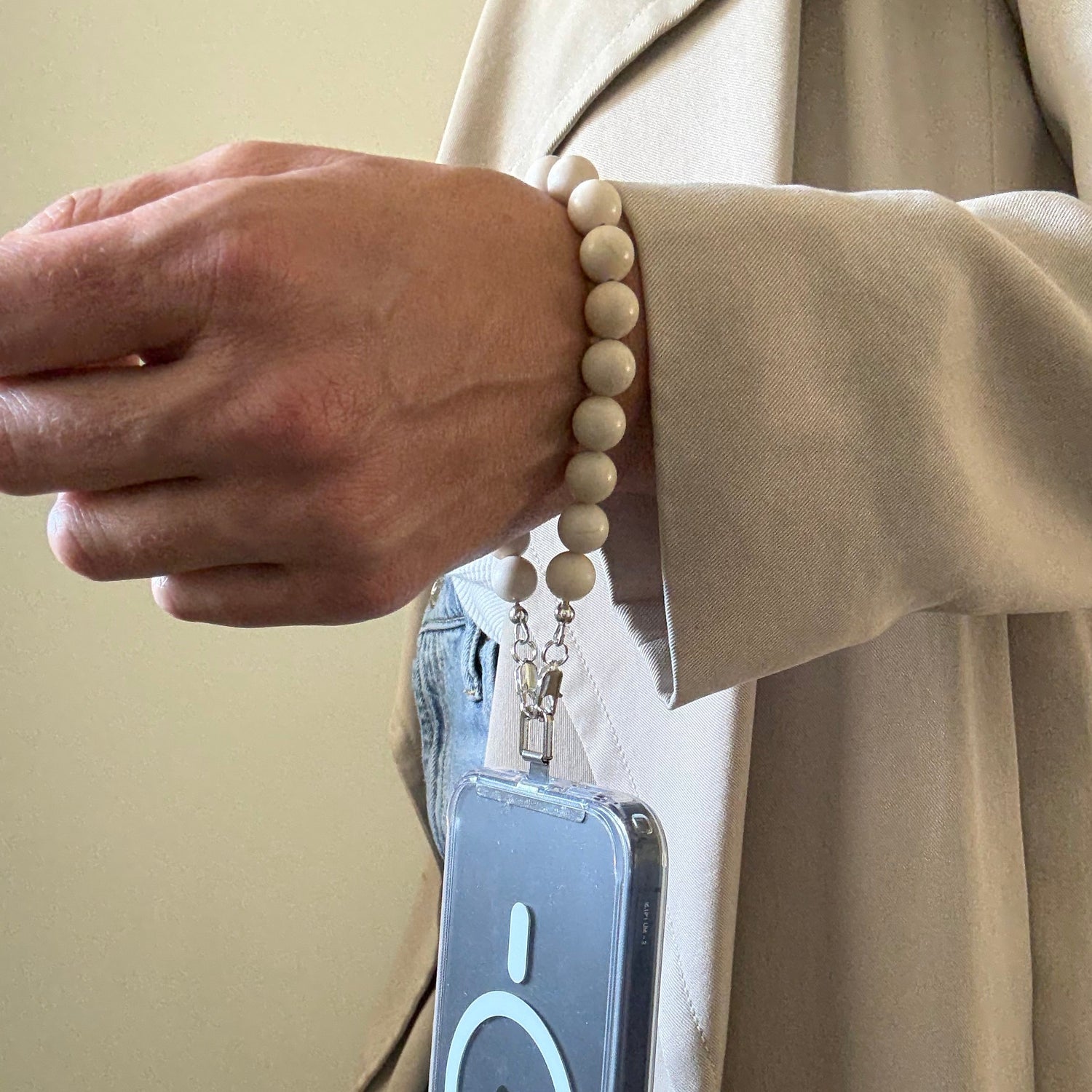 Person wearing a beige trench coat with a smarthone attached to a beaded fossil jasper phone chain.