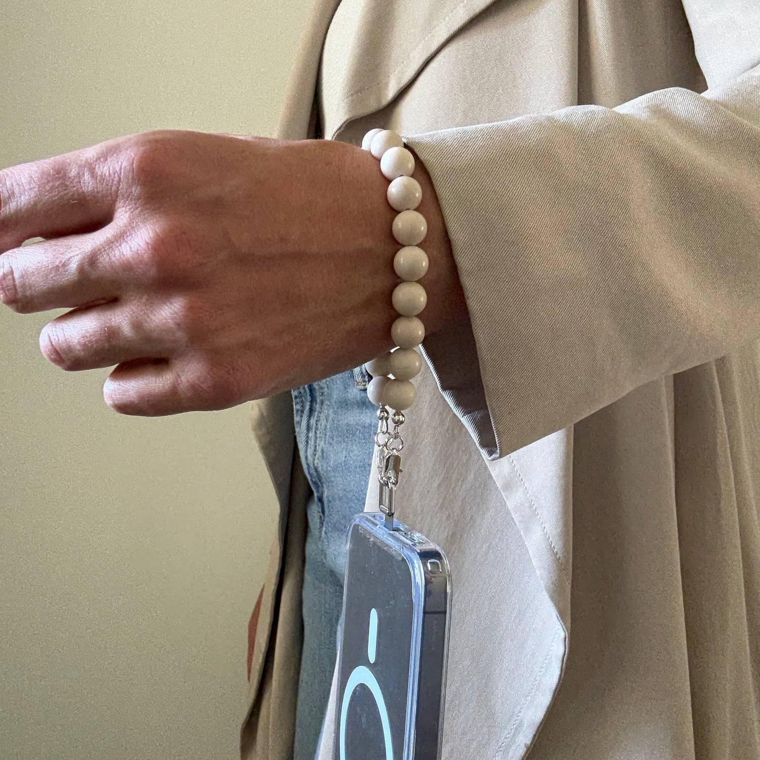 Person wearing a beige trench coat with a smarthone attached to a beaded fossil jasper phone chain.