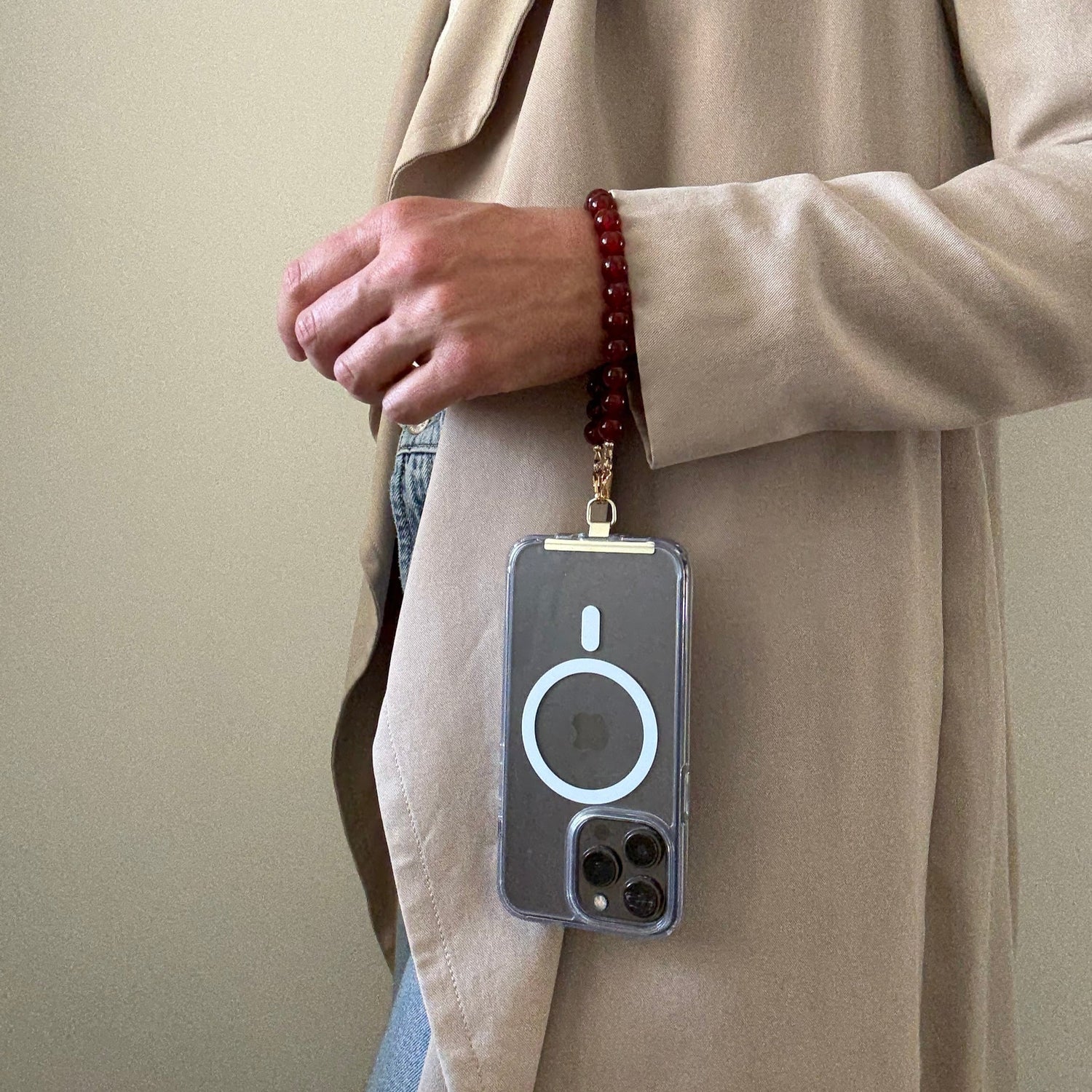 Person wearing a beige coat with a carnelian phone chain on a lanyard against a plain background