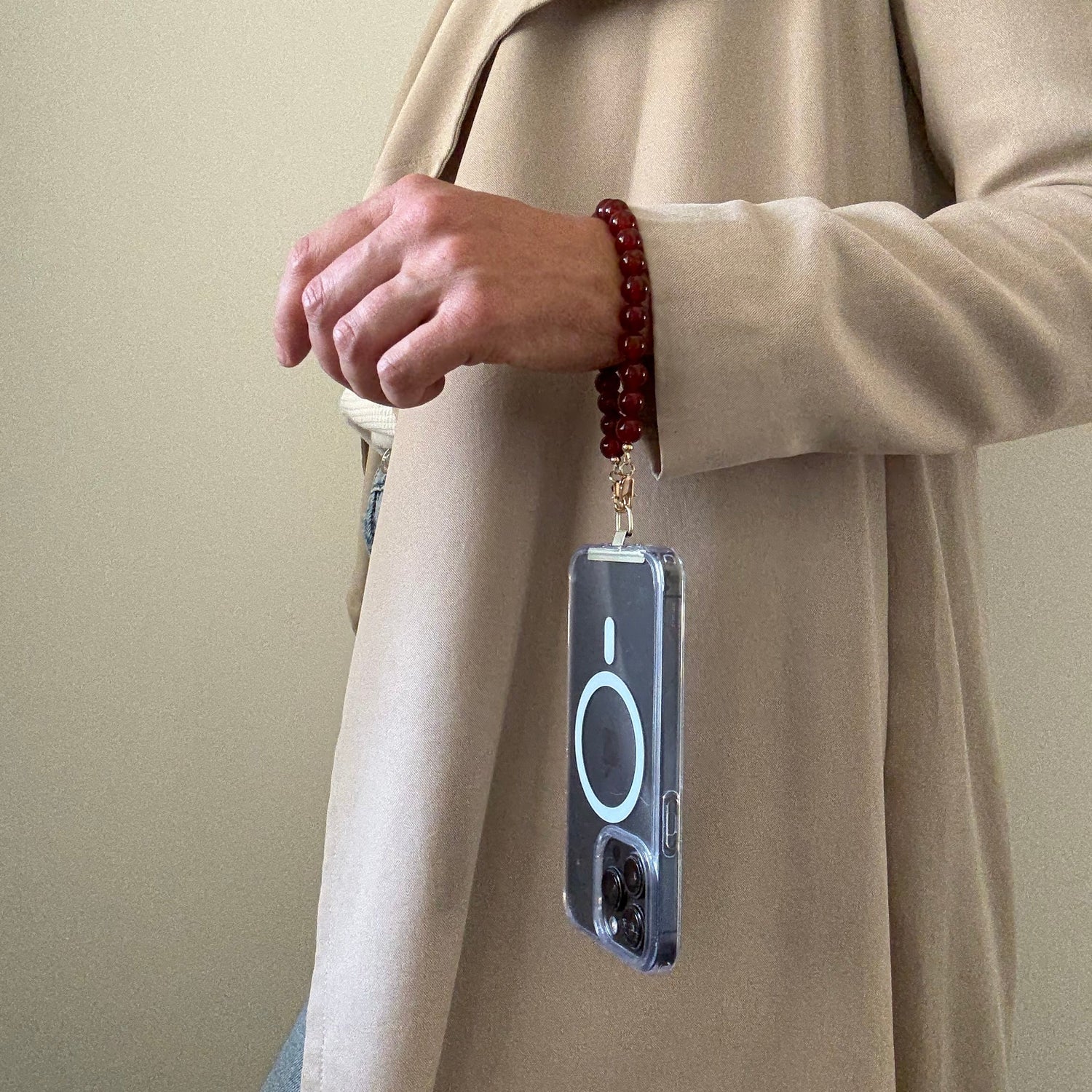 Person holding a phone with a carnelian phone chain and wearing beige coat.