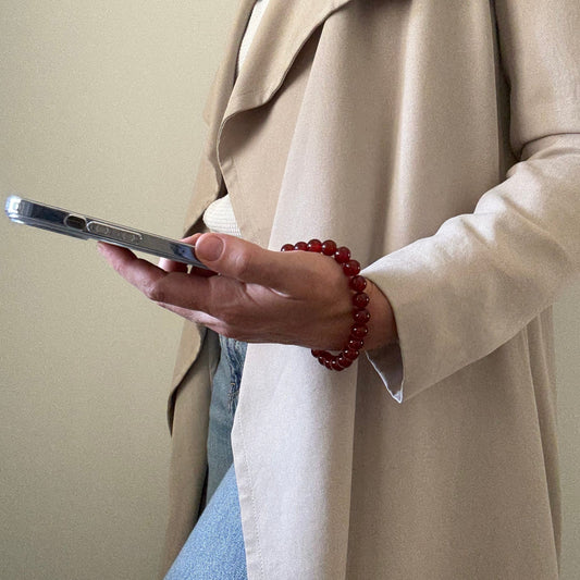 Person holding a smartphone with carnelian phone chain and wearing a beige coat.