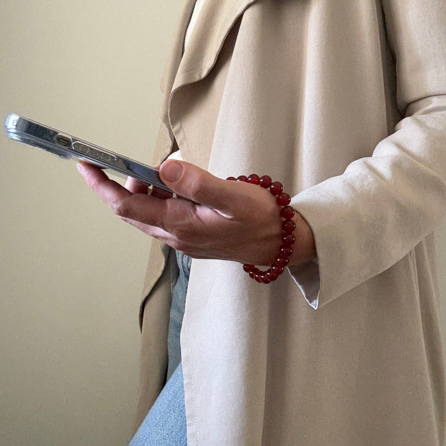 Hand holding a smartphone with a red beaded phone chain on a beige background