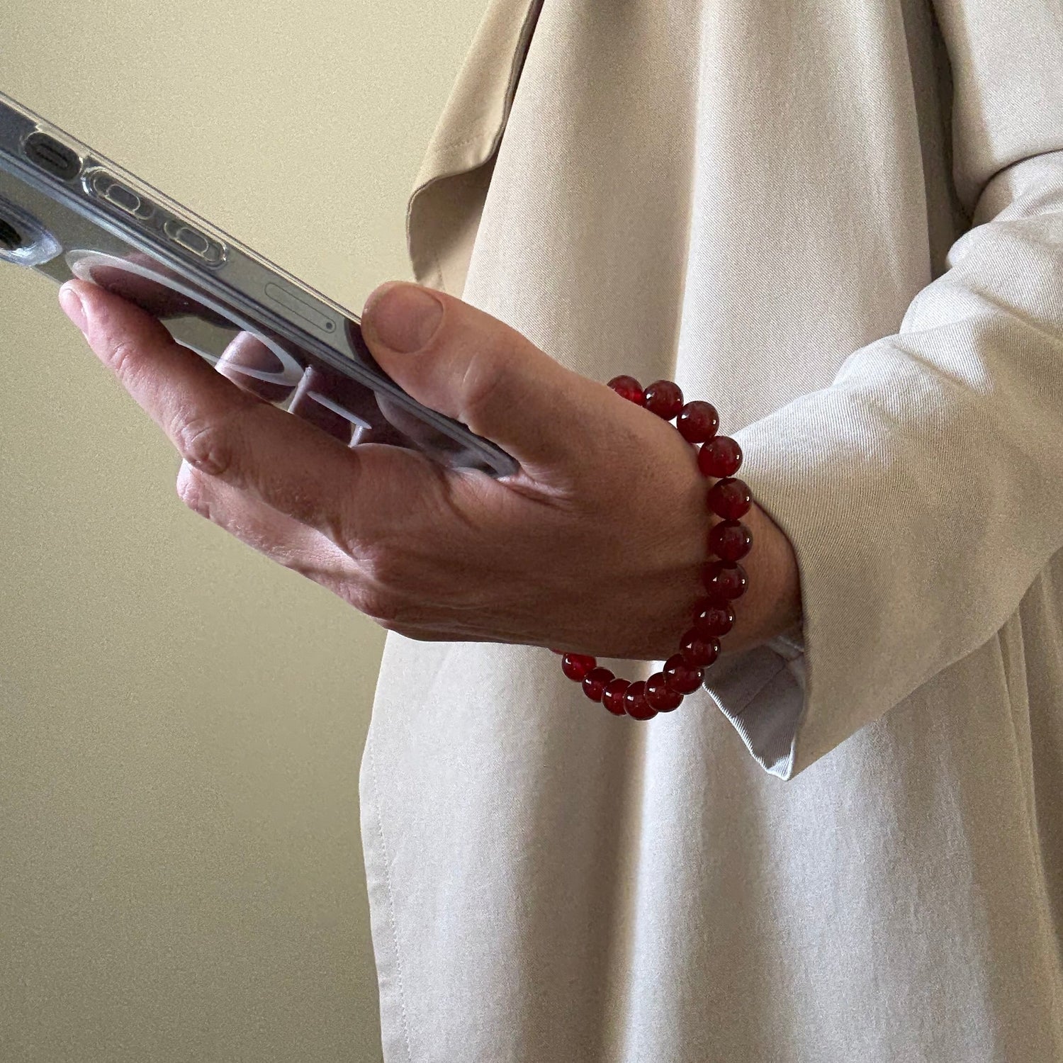 Hand holding a smartphone with a red beaded phone chain on a beige background