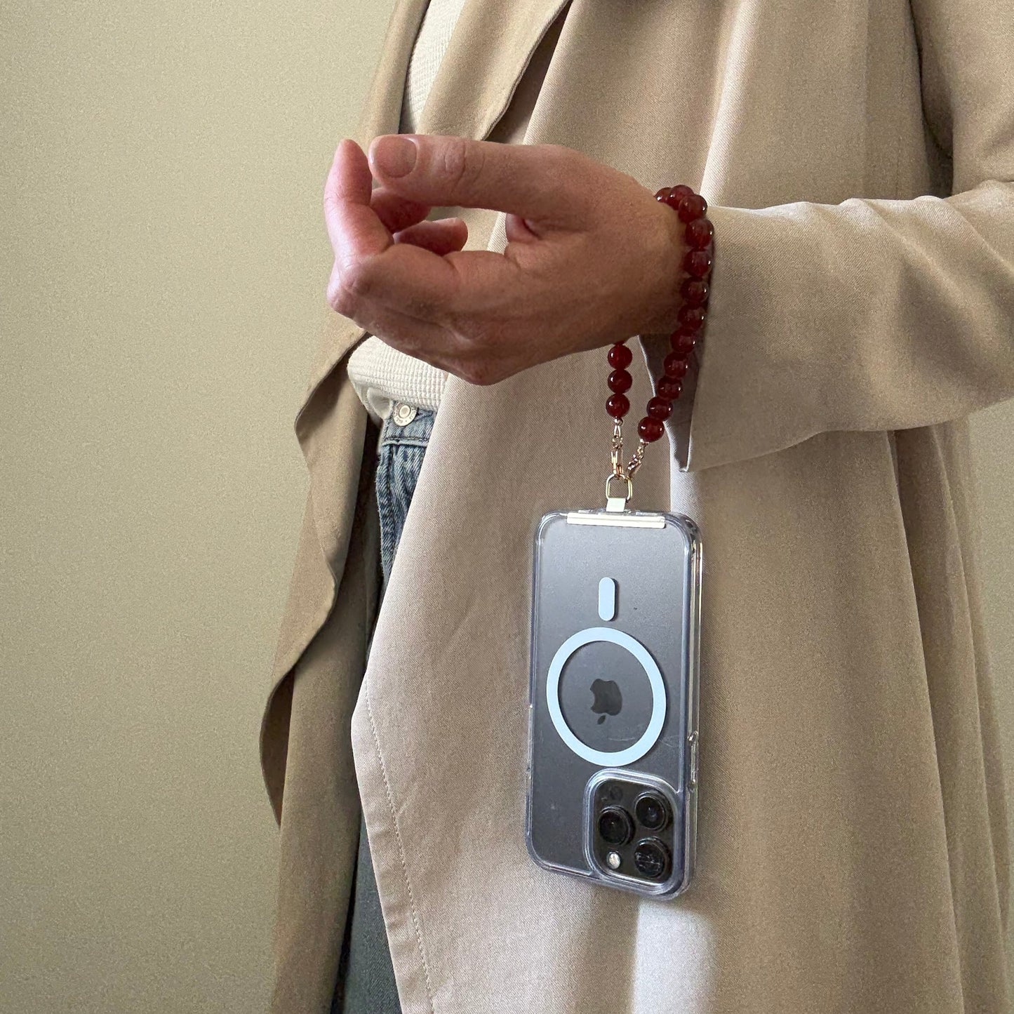 Person wearing a red beaded phone chain holding a phone with a beige background