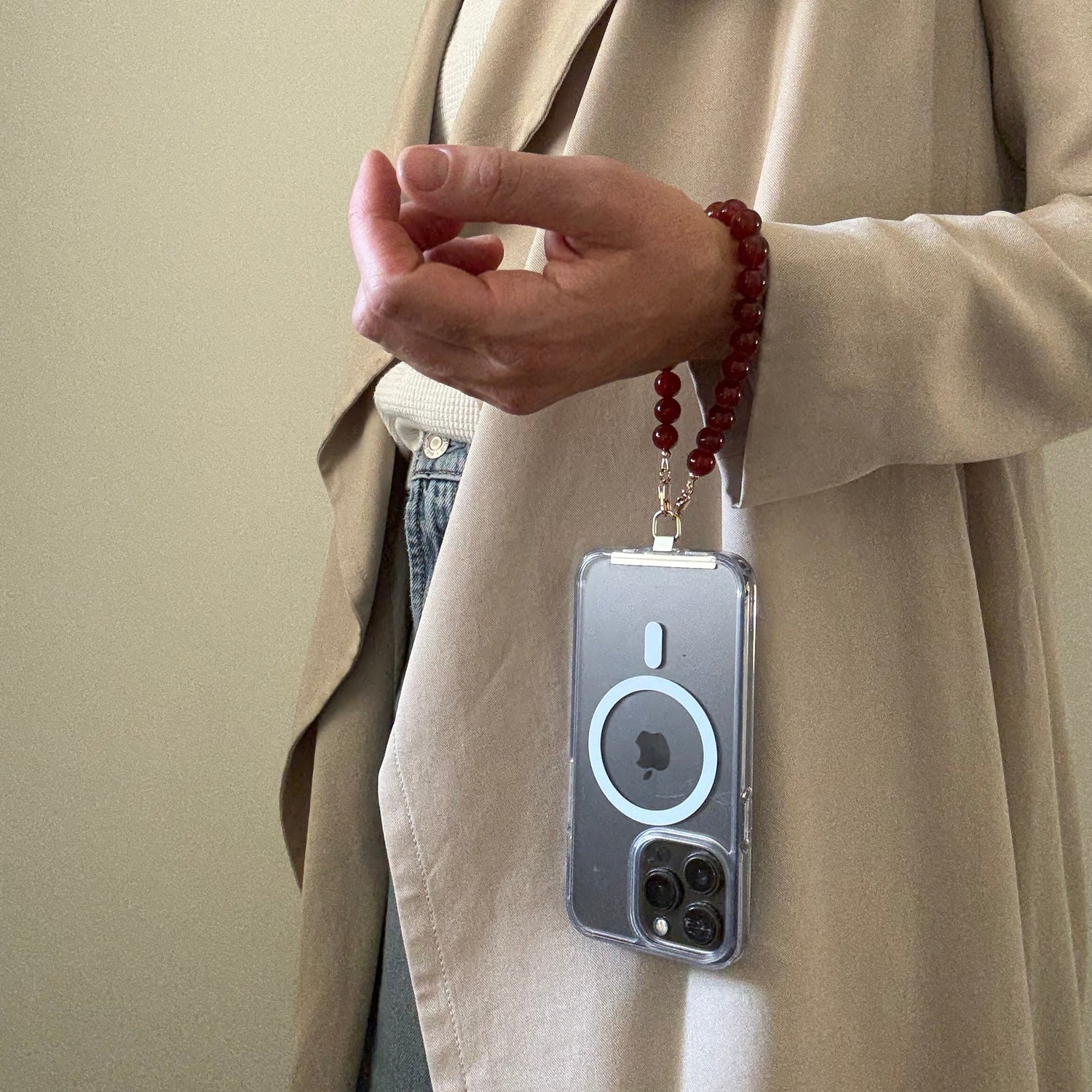 Person wearing a red beaded phone chain holding a phone with a beige background