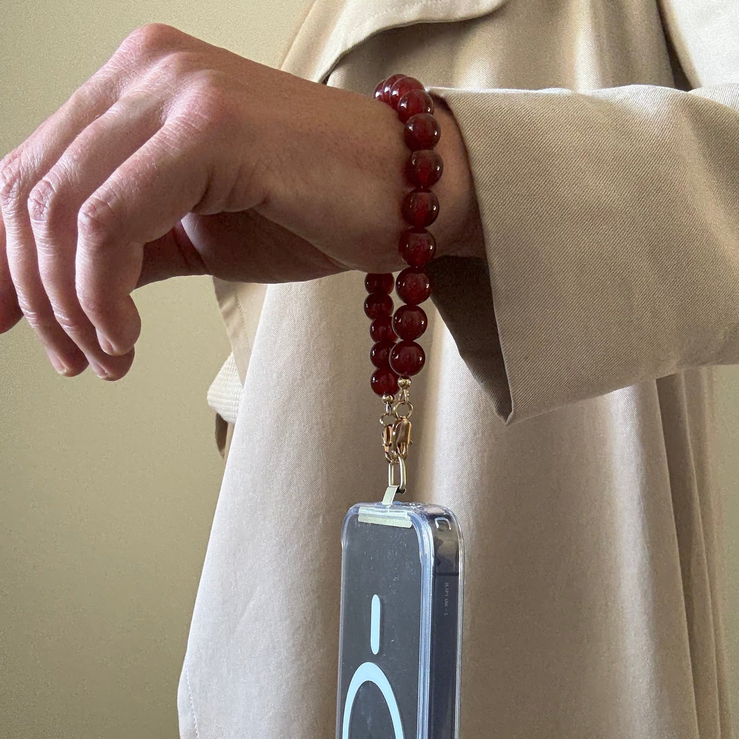 Person wearing a red beaded phone strap with a phone case on a beige background