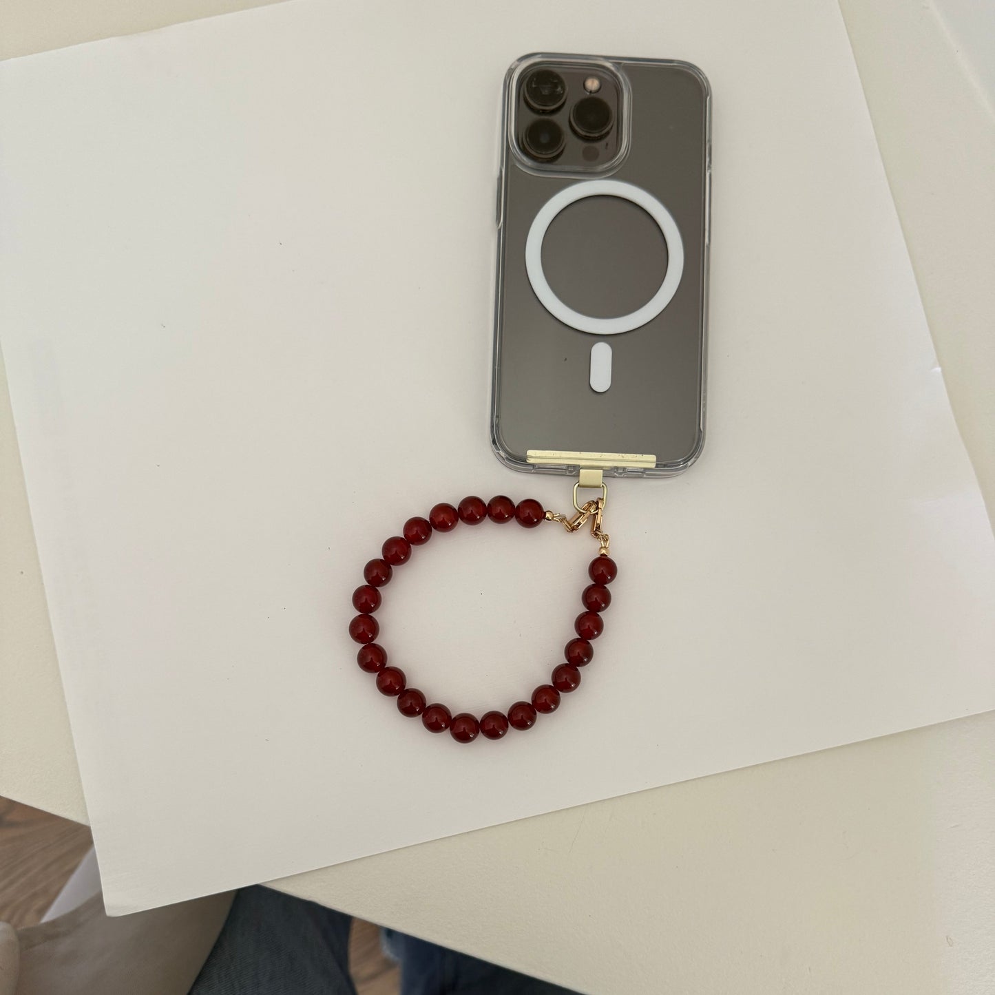 Red beaded phone chain on a white surface next to a smartphone with a case.