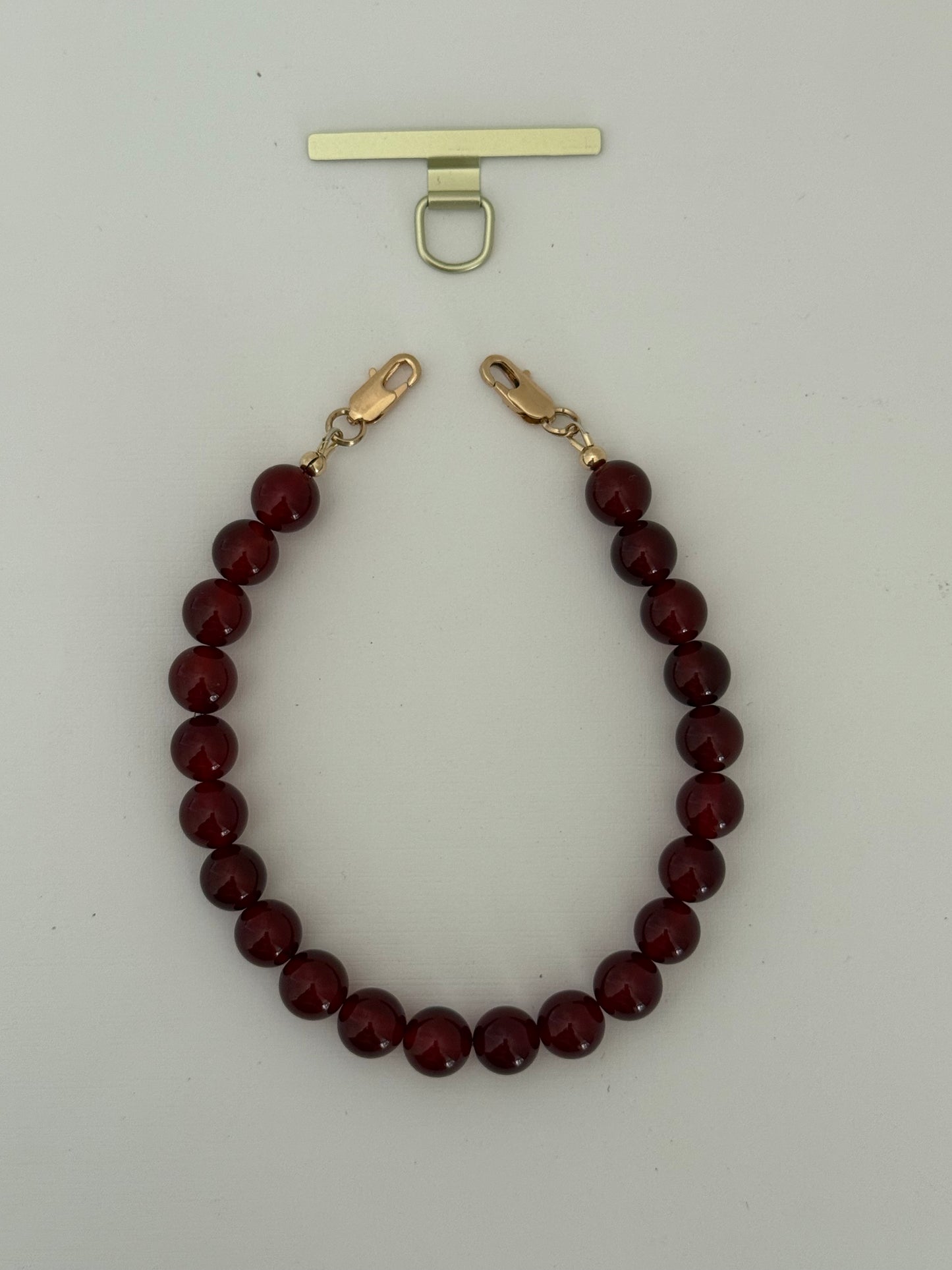 Red beaded phone chain with gold clasp on a light gray background
