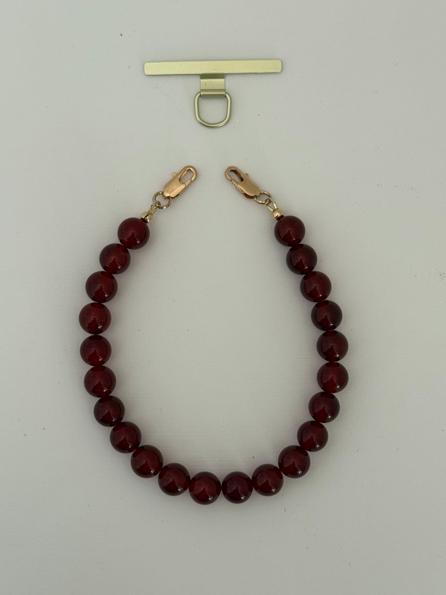 Red beaded phone chain with gold clasp on a light gray background