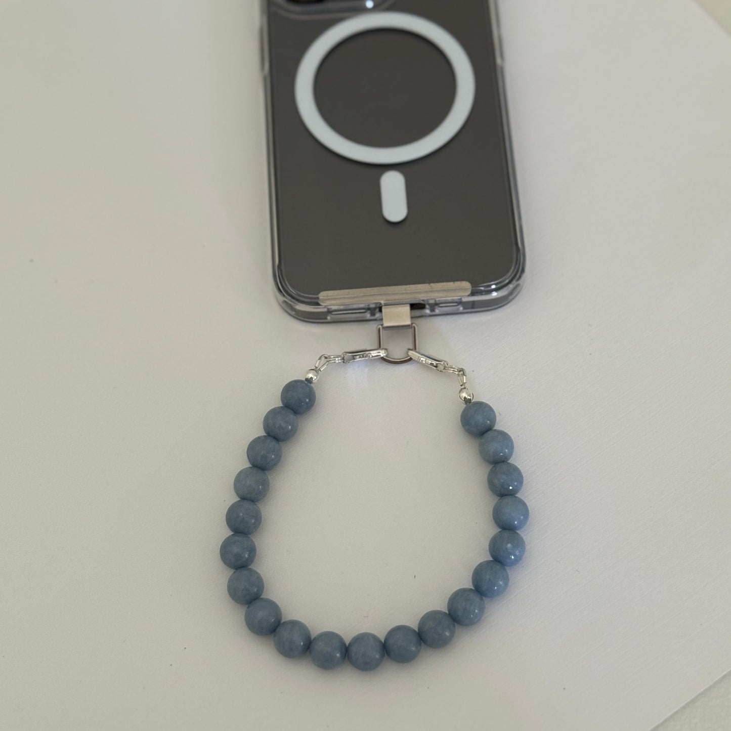 Blue beaded mobile phone chain on a white surface with a phone case in the background