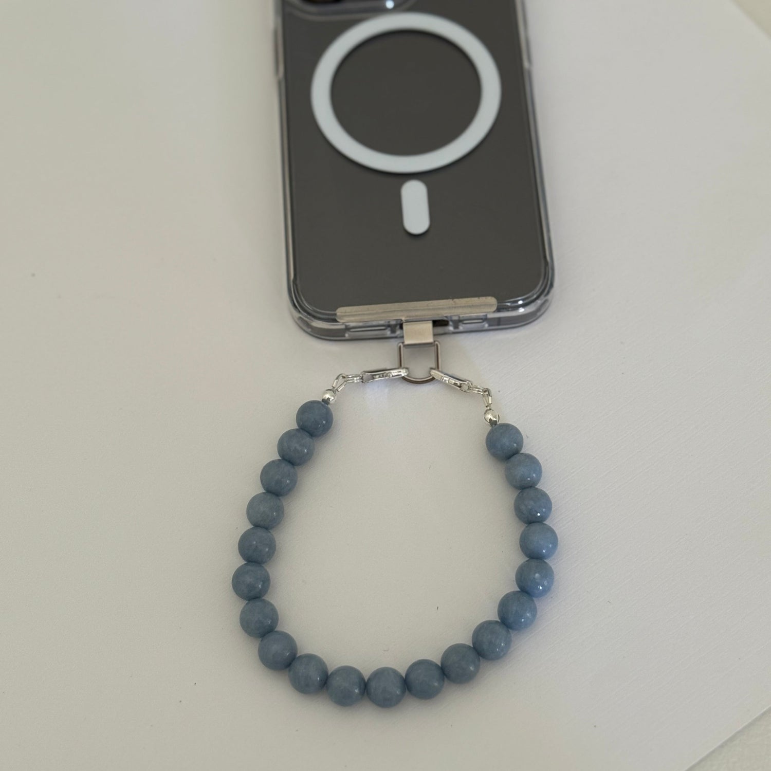 Blue beaded mobile phone chain on a white surface with a phone case in the background