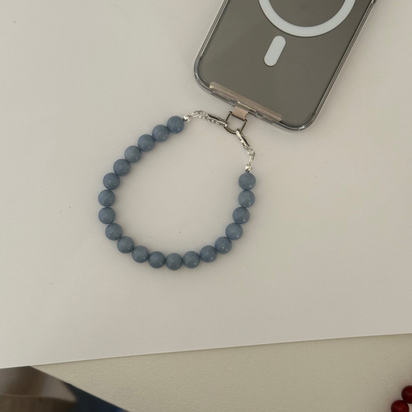 Blue beaded mobile phone chain on a white surface with an Apple device in the background