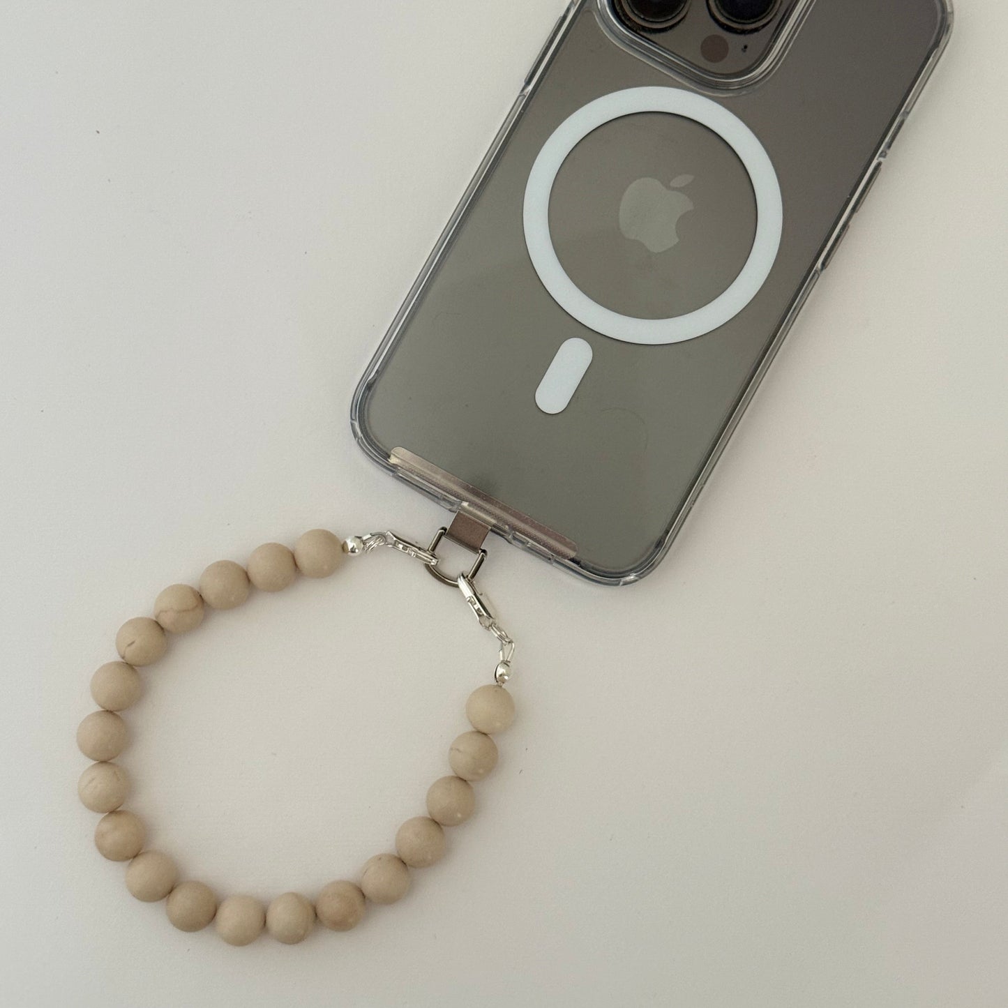 Smartphone with clear case and a beaded beige phone chain on a white background