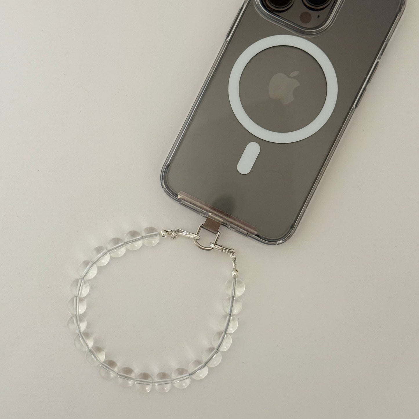 Smartphone with clear quartz beaded phone chain on a light gray background