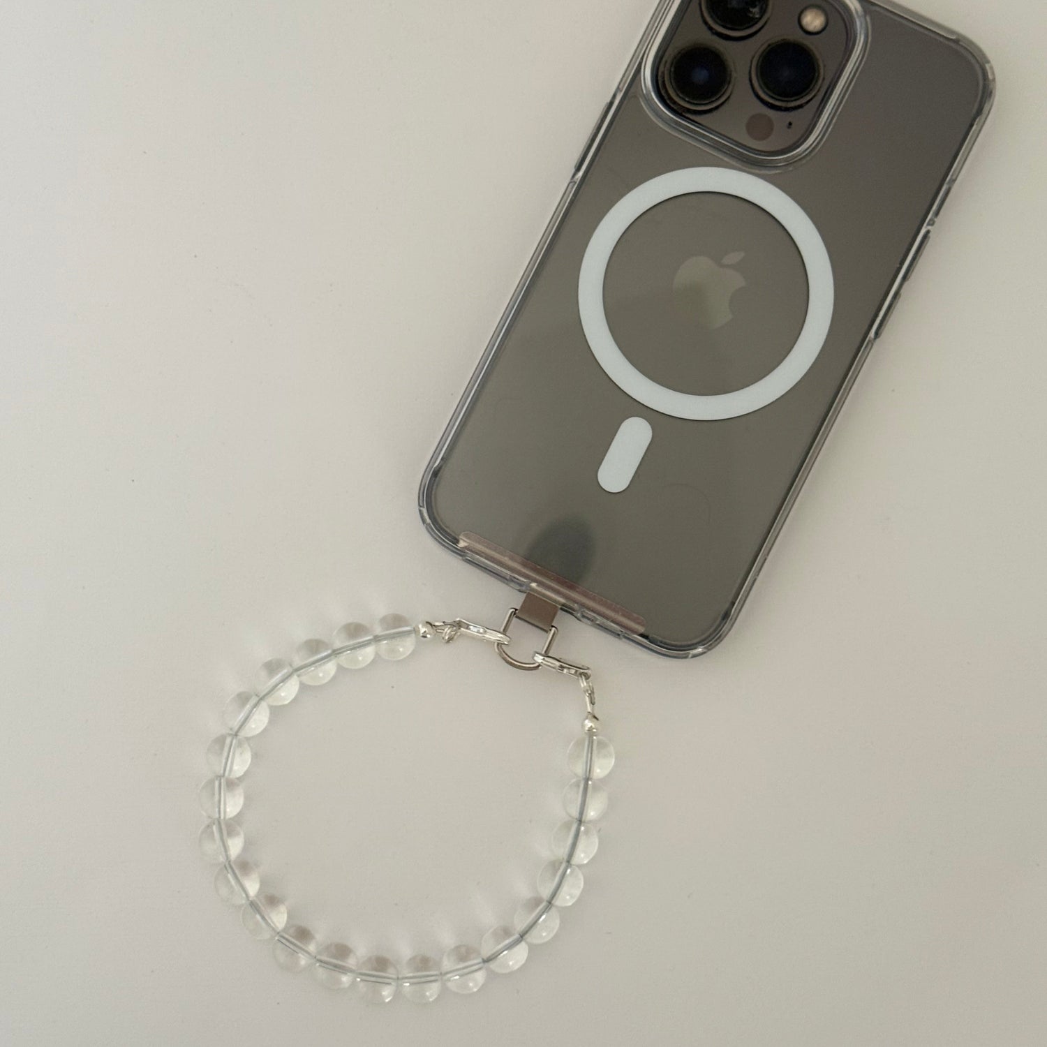 Smartphone with a beaded clear quartz crystal phone chain on a light gray background