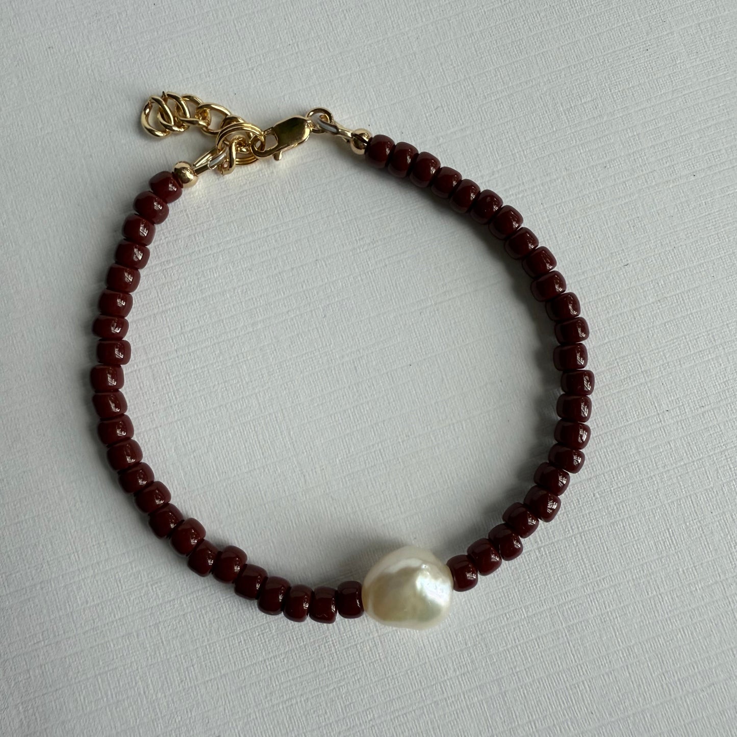 Beaded bracelet with a pearl and gold charm on a light gray background