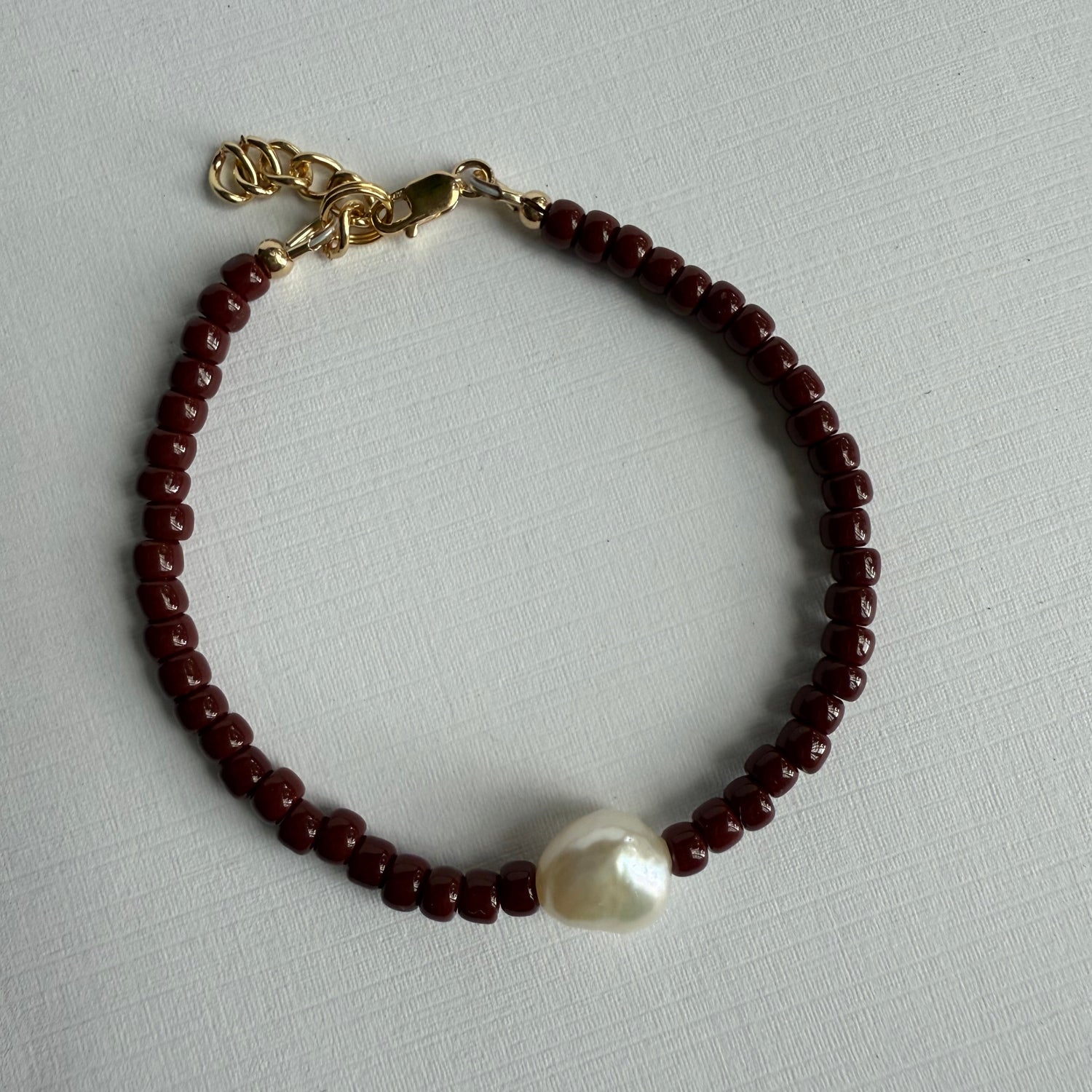 Beaded bracelet with a pearl and gold charm on a light gray background