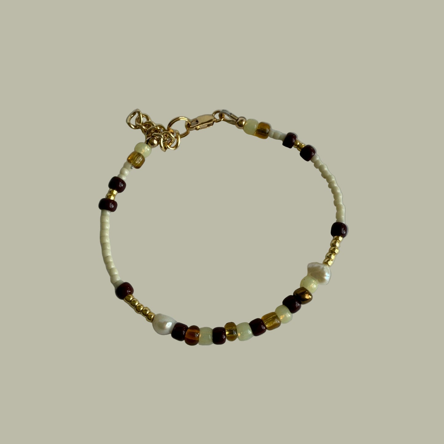 Beaded bracelet with gold charm on a light gray background