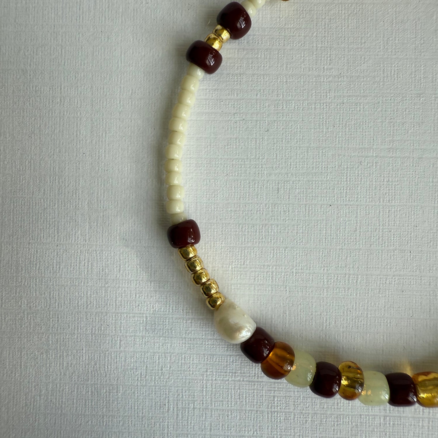 Necklace with white, brown, and gold beads on a light gray background