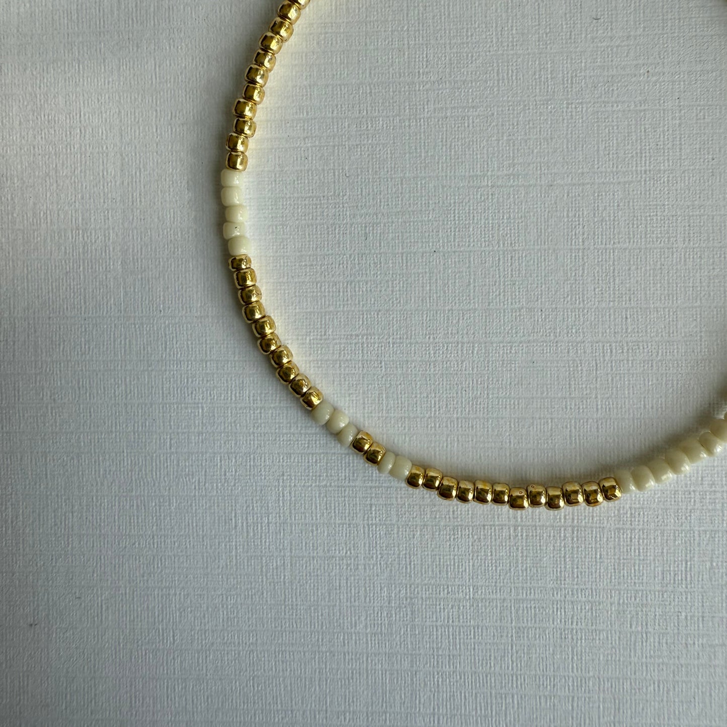 Necklace with gold and white beads on a light gray background