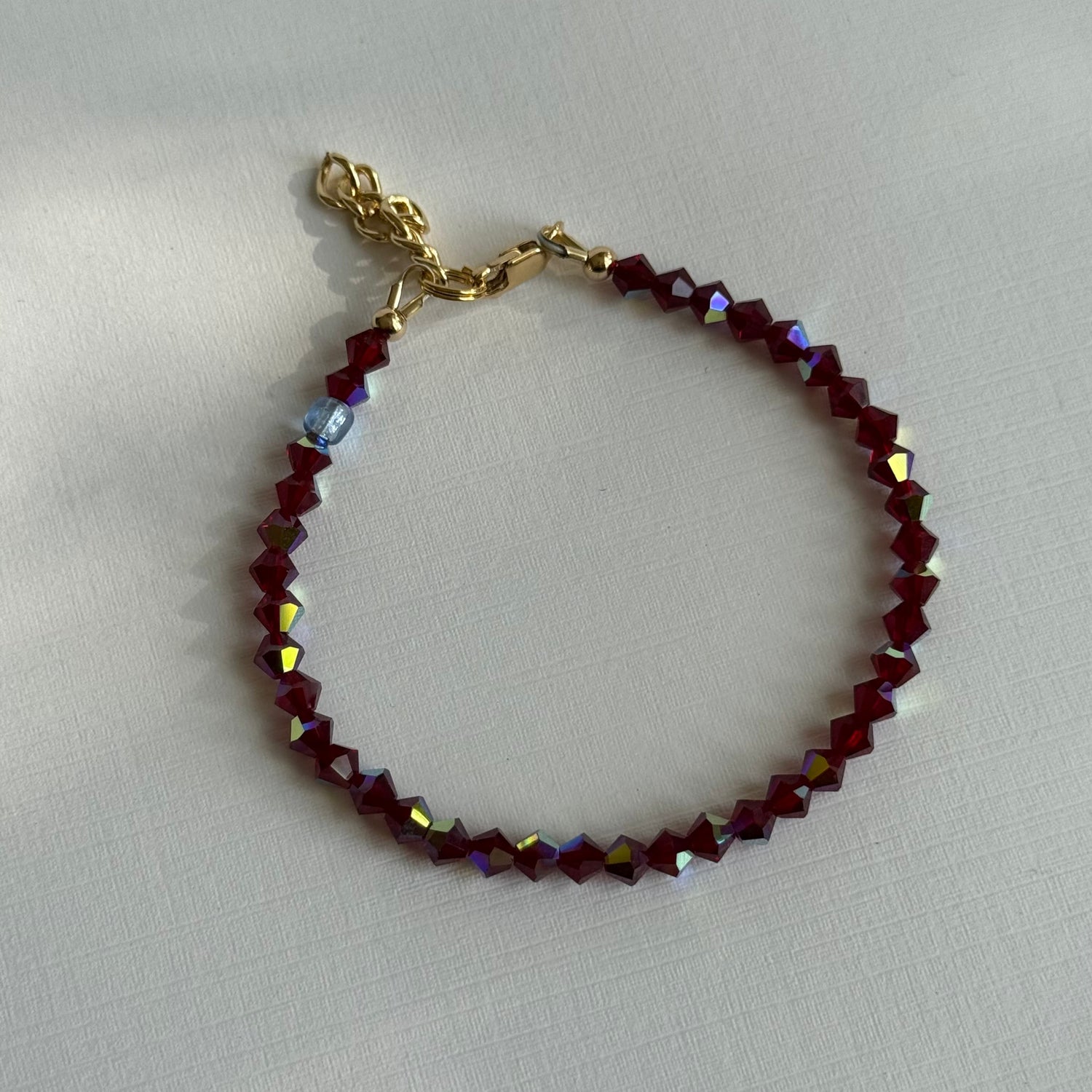 Bracelet with red beads and gold clasp on a light gray background