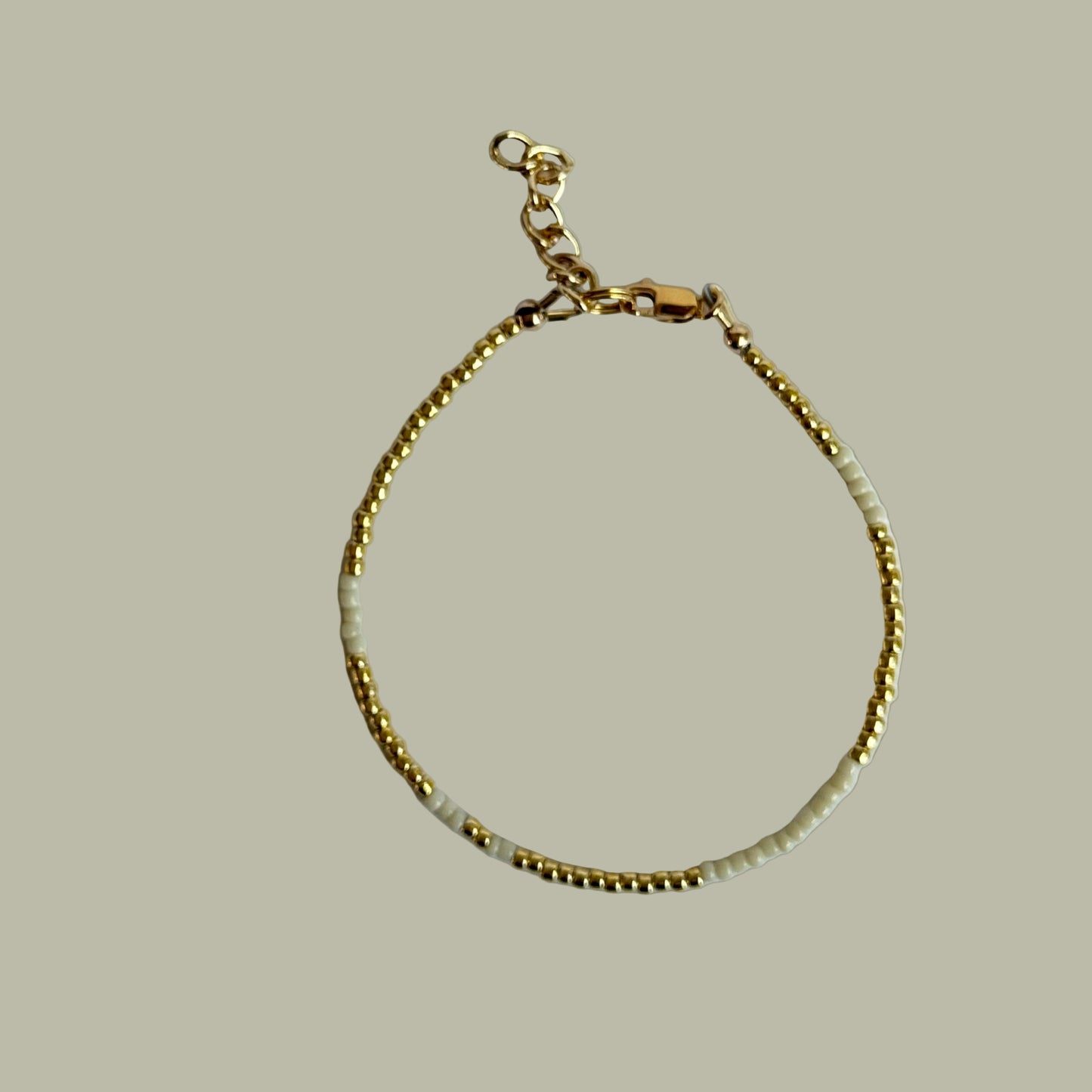 Gold bracelet with white beads on a light gray background