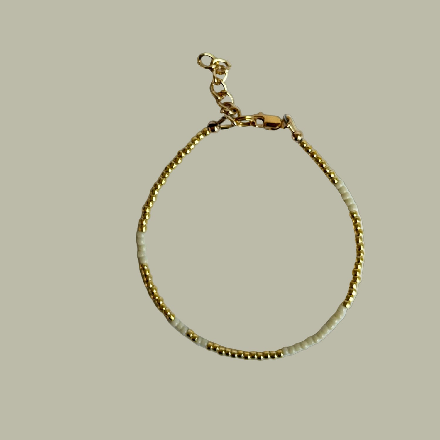 Gold bracelet with white beads on a light gray background
