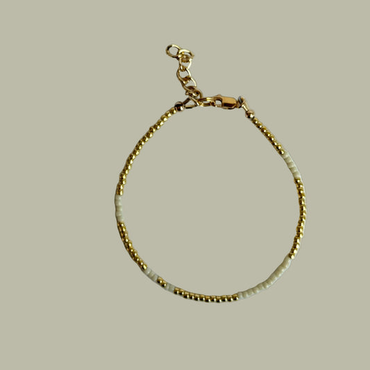 Gold bracelet with white beads on a light gray background