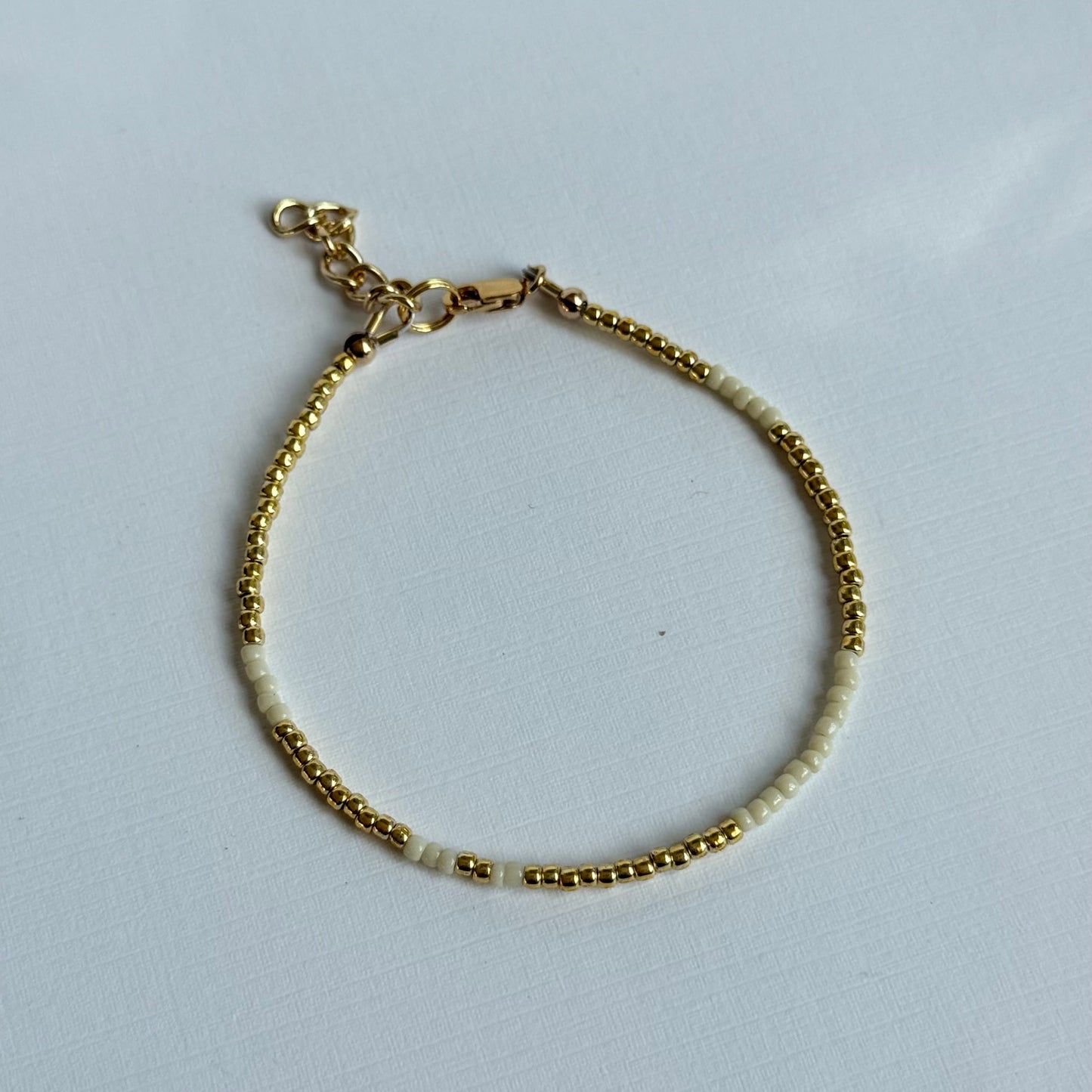 Gold bracelet with small beads on a light gray background