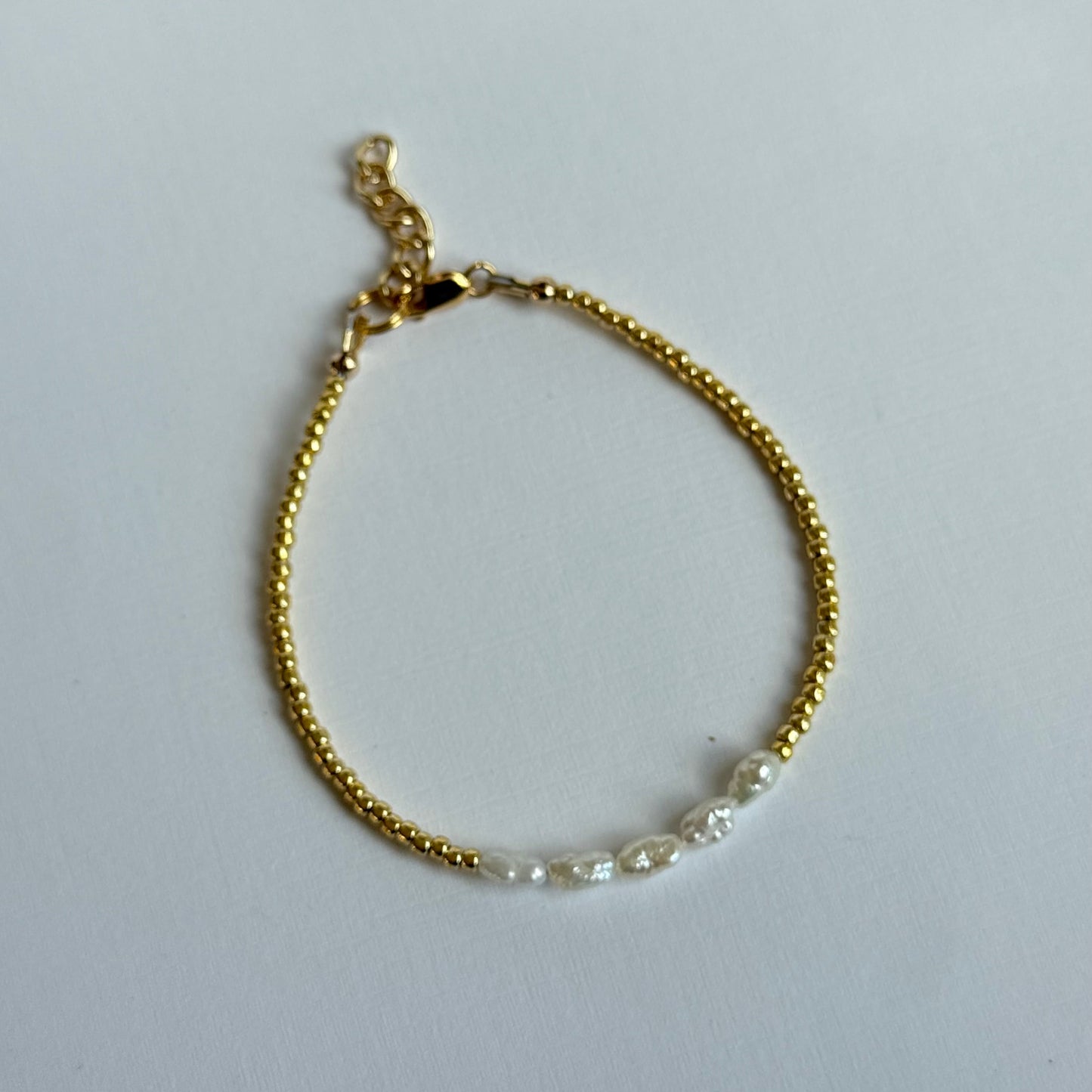Gold bracelet with pearls on a light gray background