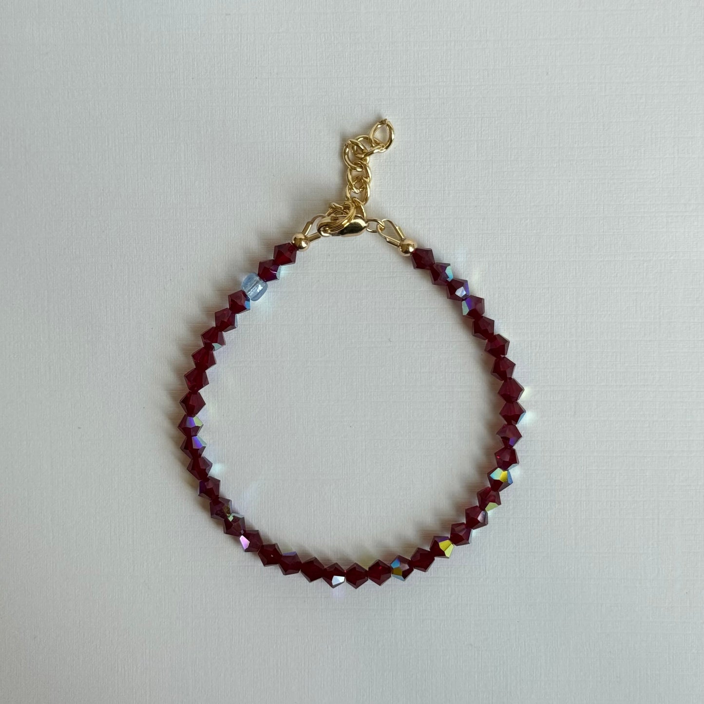 Bracelet with red beads and gold clasp on a light gray background