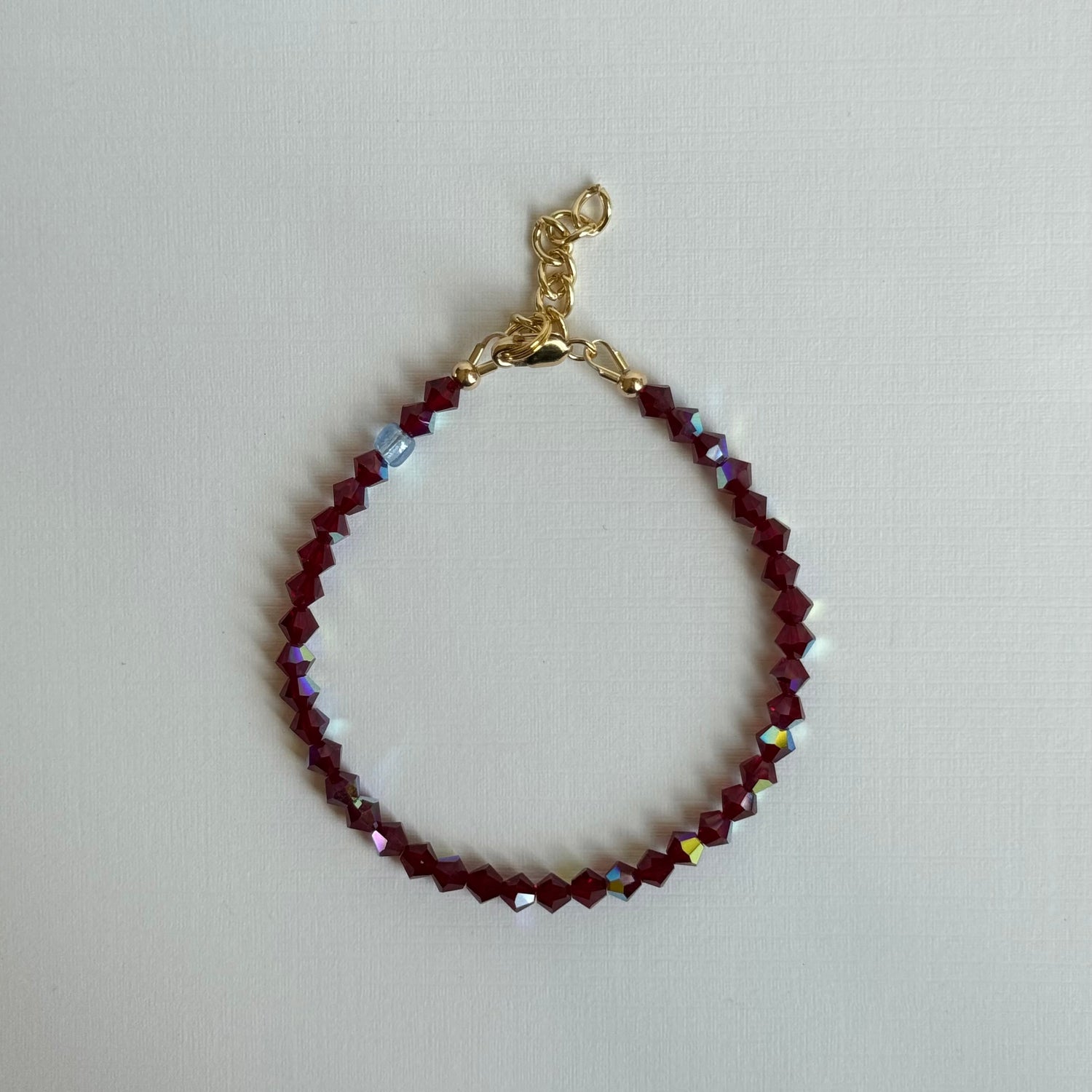 Bracelet with red beads and gold clasp on a light gray background