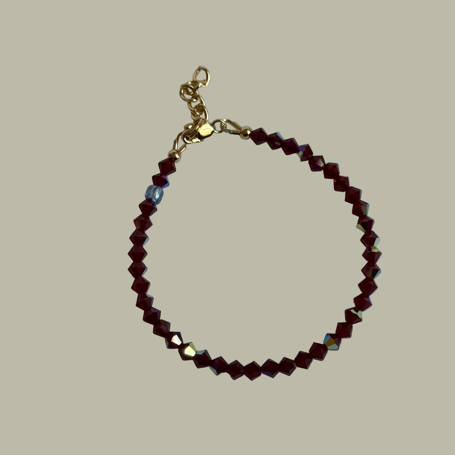 Bracelet with red beads and gold clasp on a light gray background