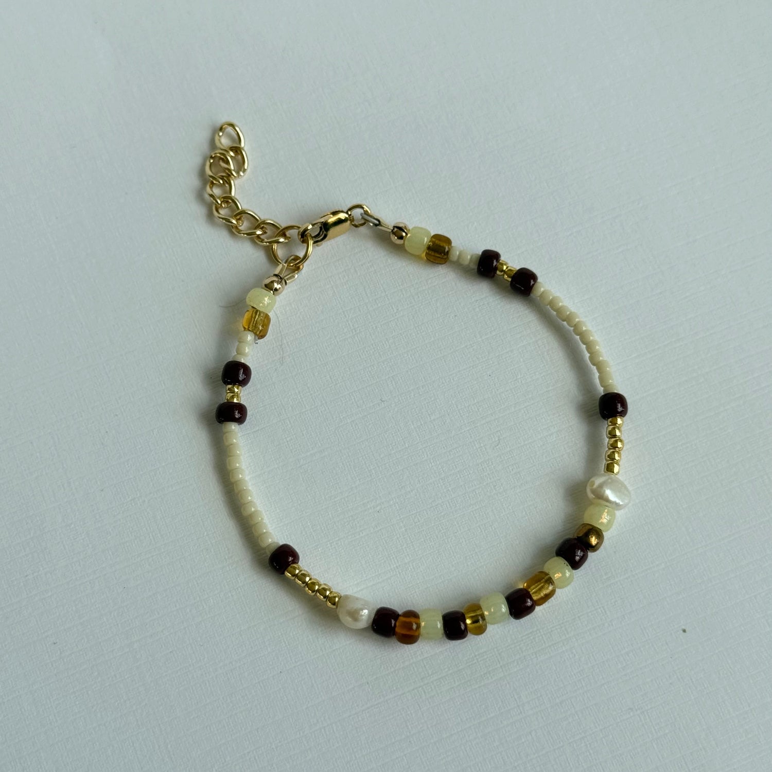 Beaded bracelet with gold chain on a light gray background